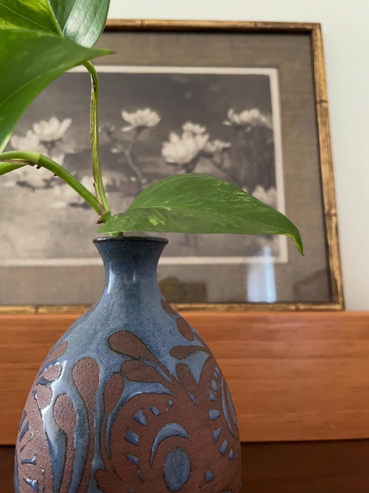 Decorative blue vase with floral patterns in front of a framed black and white print on a wooden surface.