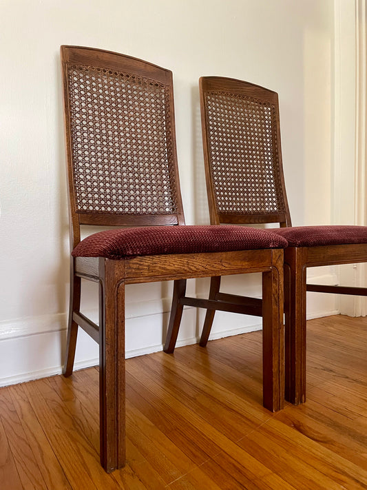 Two wooden chairs with cane backs and red cushions on a wooden floor.