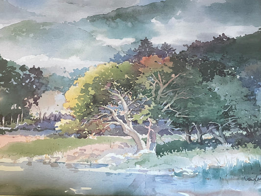 Watercolor landscape painting featuring a tree by a body of water, with green and yellow foliage, dark forested hills, and a cloudy sky.