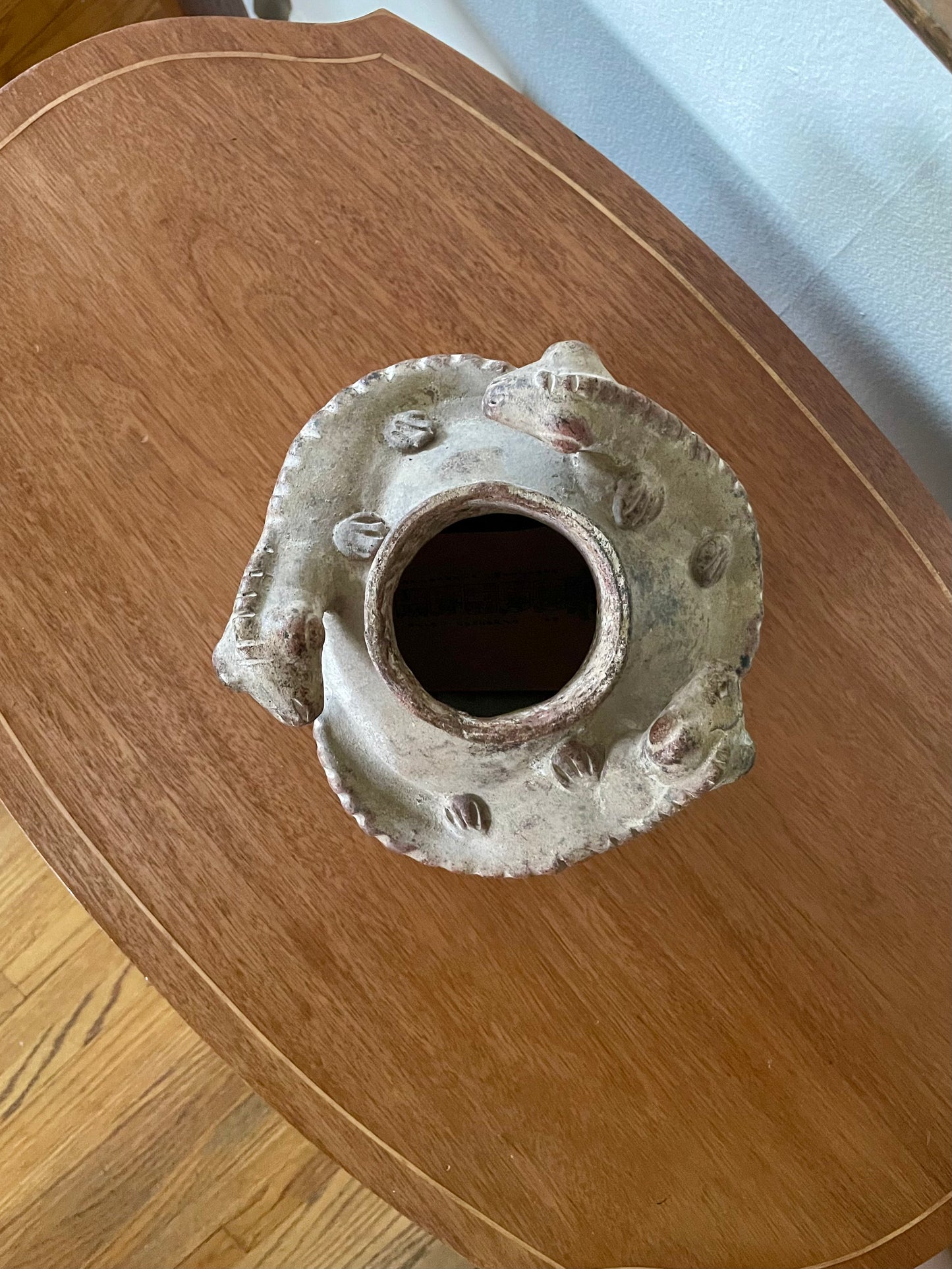 A handmade ceramic pot with a rustic, textured surface and raised lizard details, photographed from above on a wooden surface.