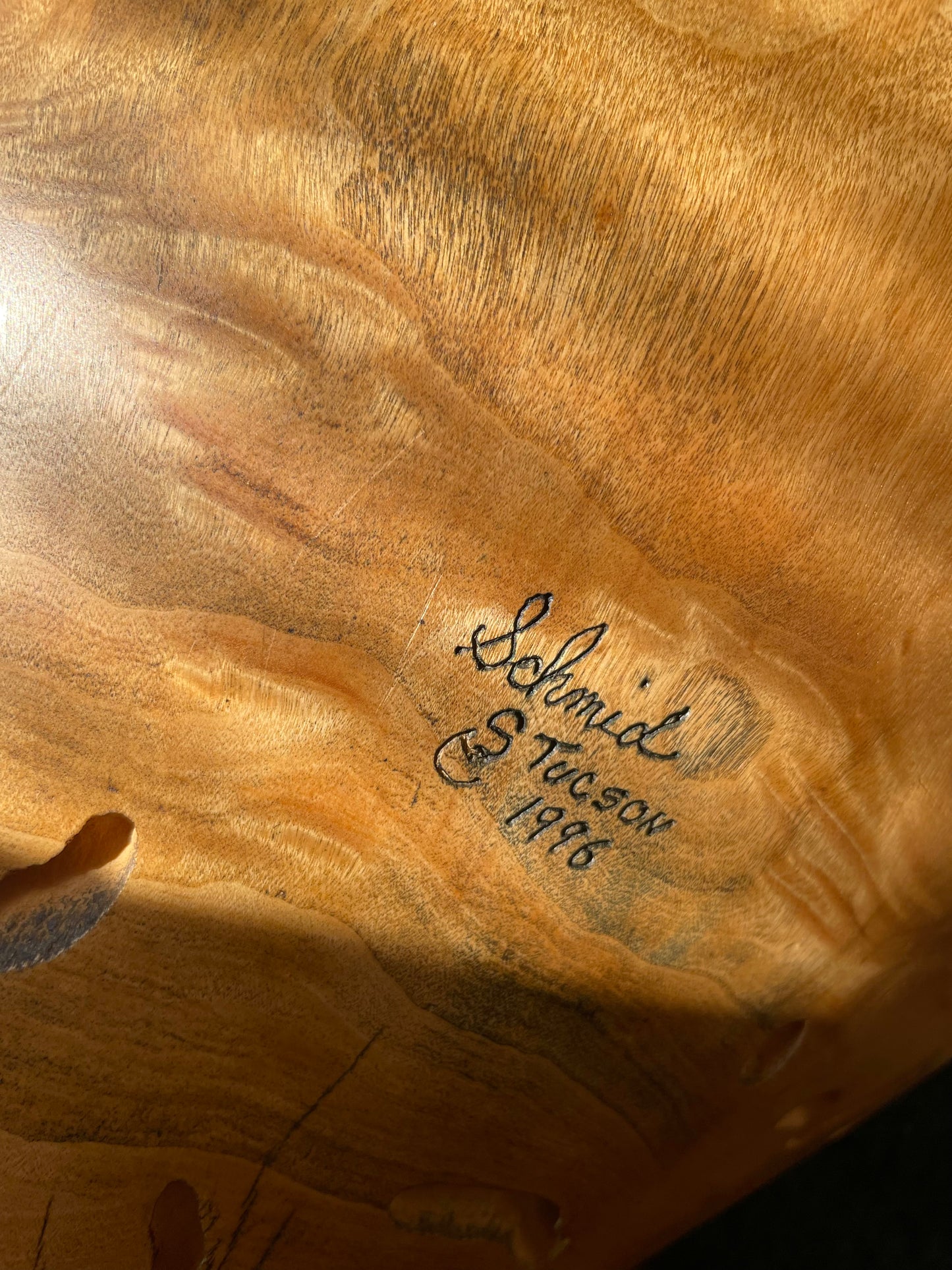 Close-up of a polished wood surface with natural grain and a handwritten signature reading ’Schmid, S. Tucson 1996'.