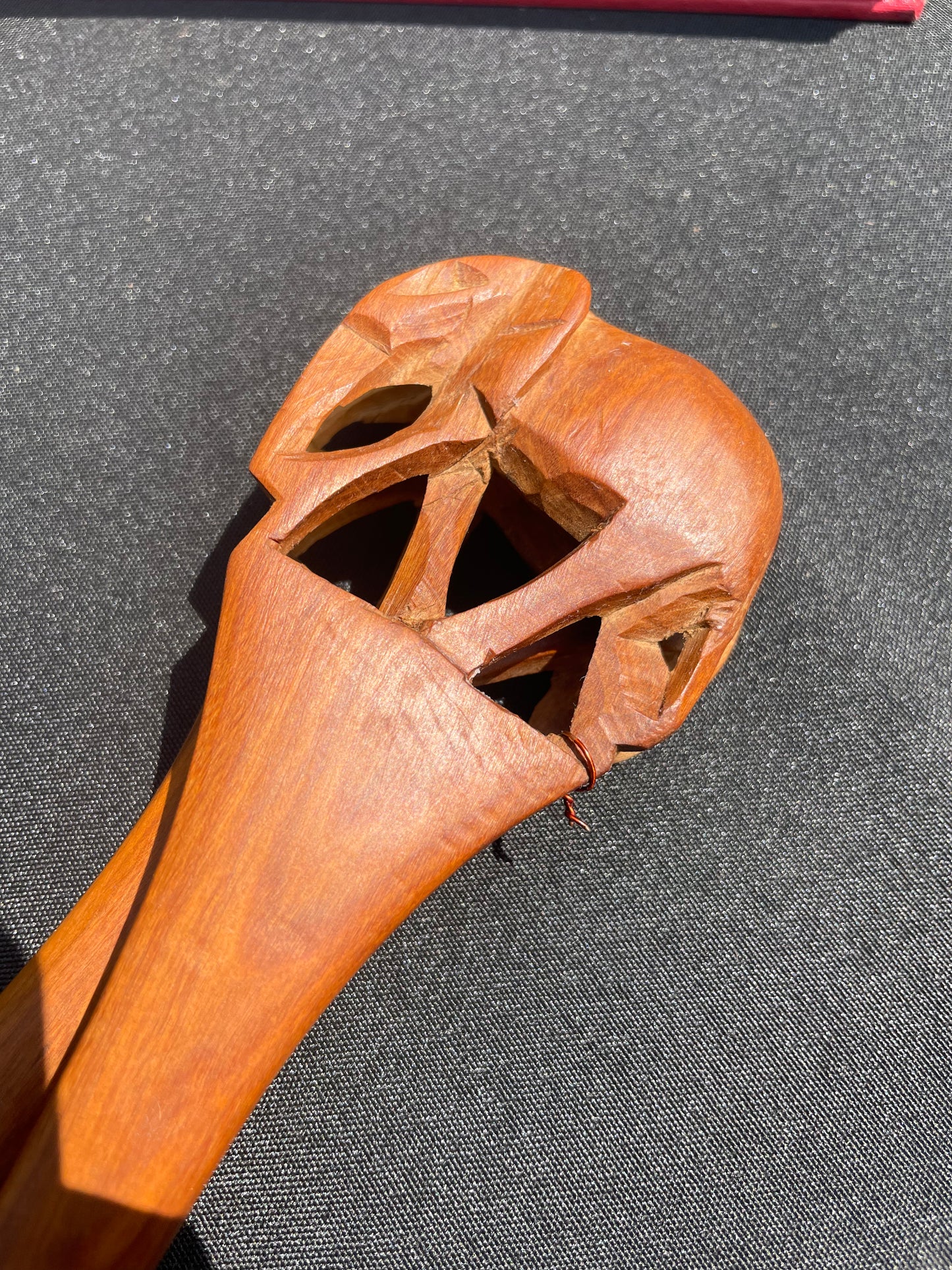 Closeup of the top of a wood spoon, featuring a hand carved elephant, resting on a black surface.