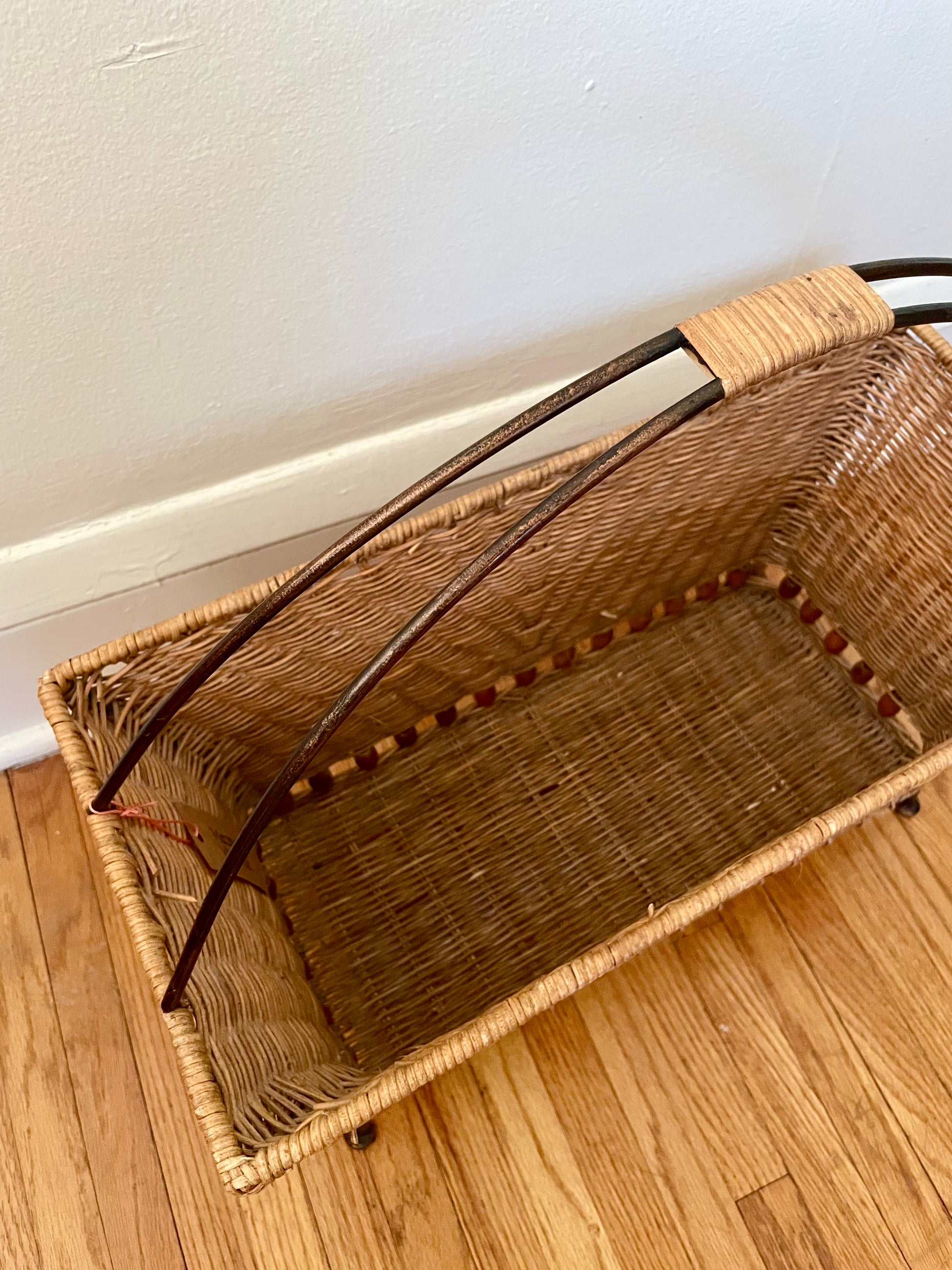 Wicker magazine basket on a wooden floor against a white wall.