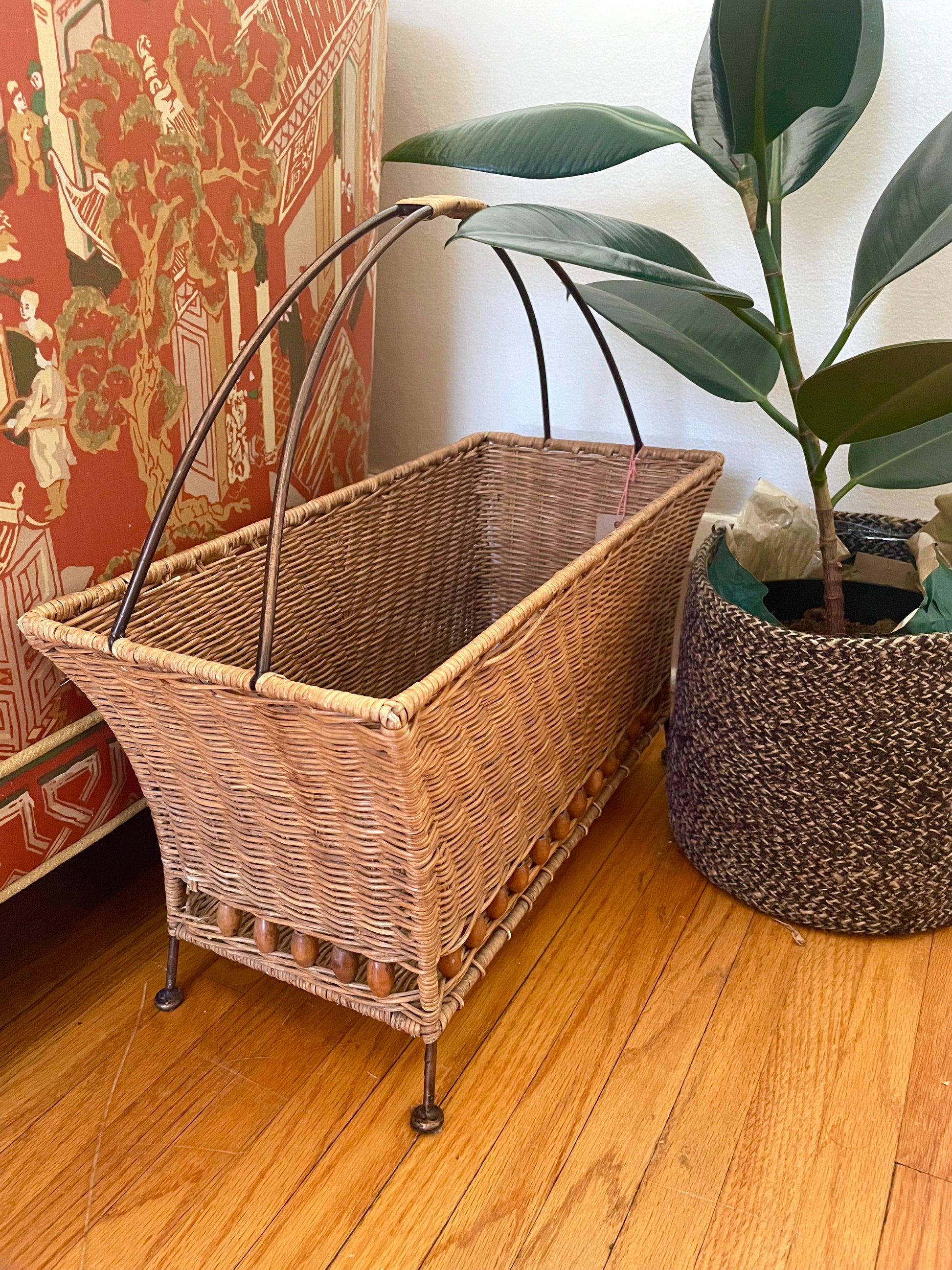 Wicker basket with handles on a wooden floor next to a plant