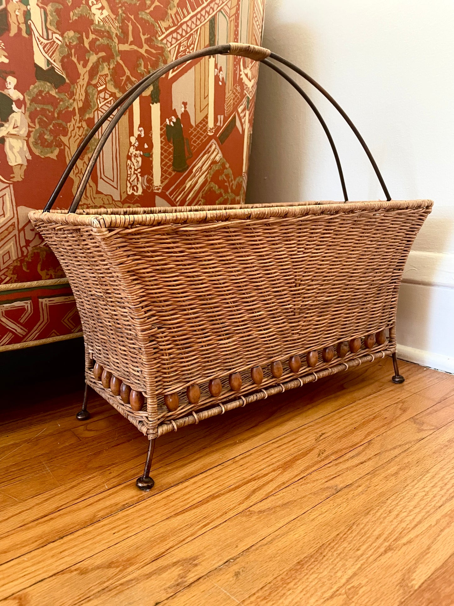 Wicker magazine basket on a wooden floor next to a couch with decorative upholstery.