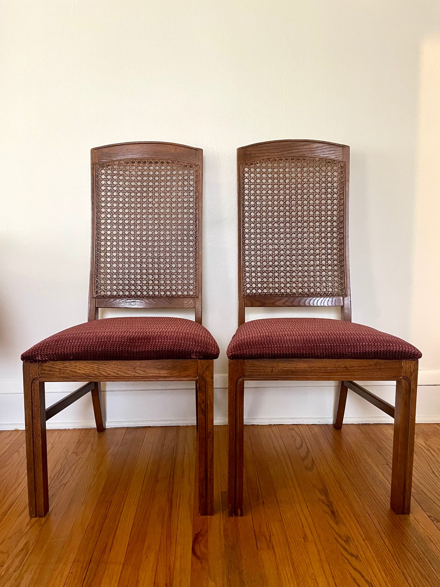 Two wooden chairs with cane backs and red cushioned seats on a wooden floor.
