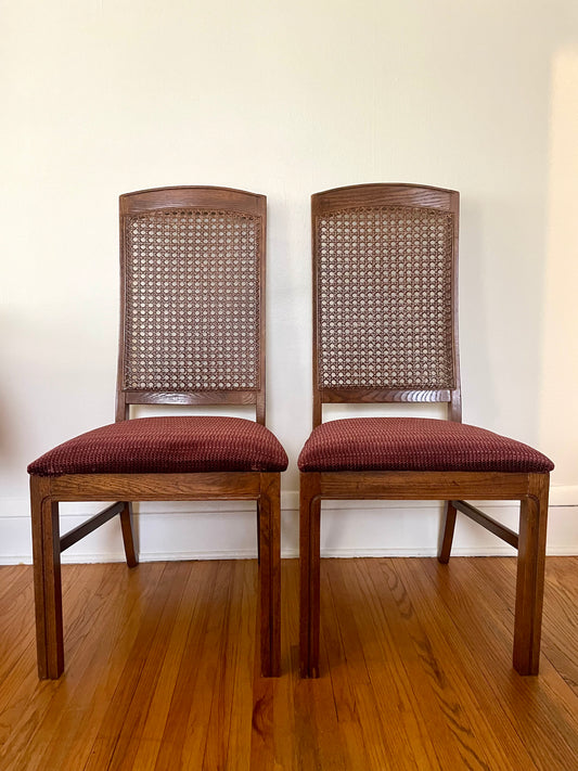 Two wooden chairs with cane backs and red cushioned seats on a wooden floor.
