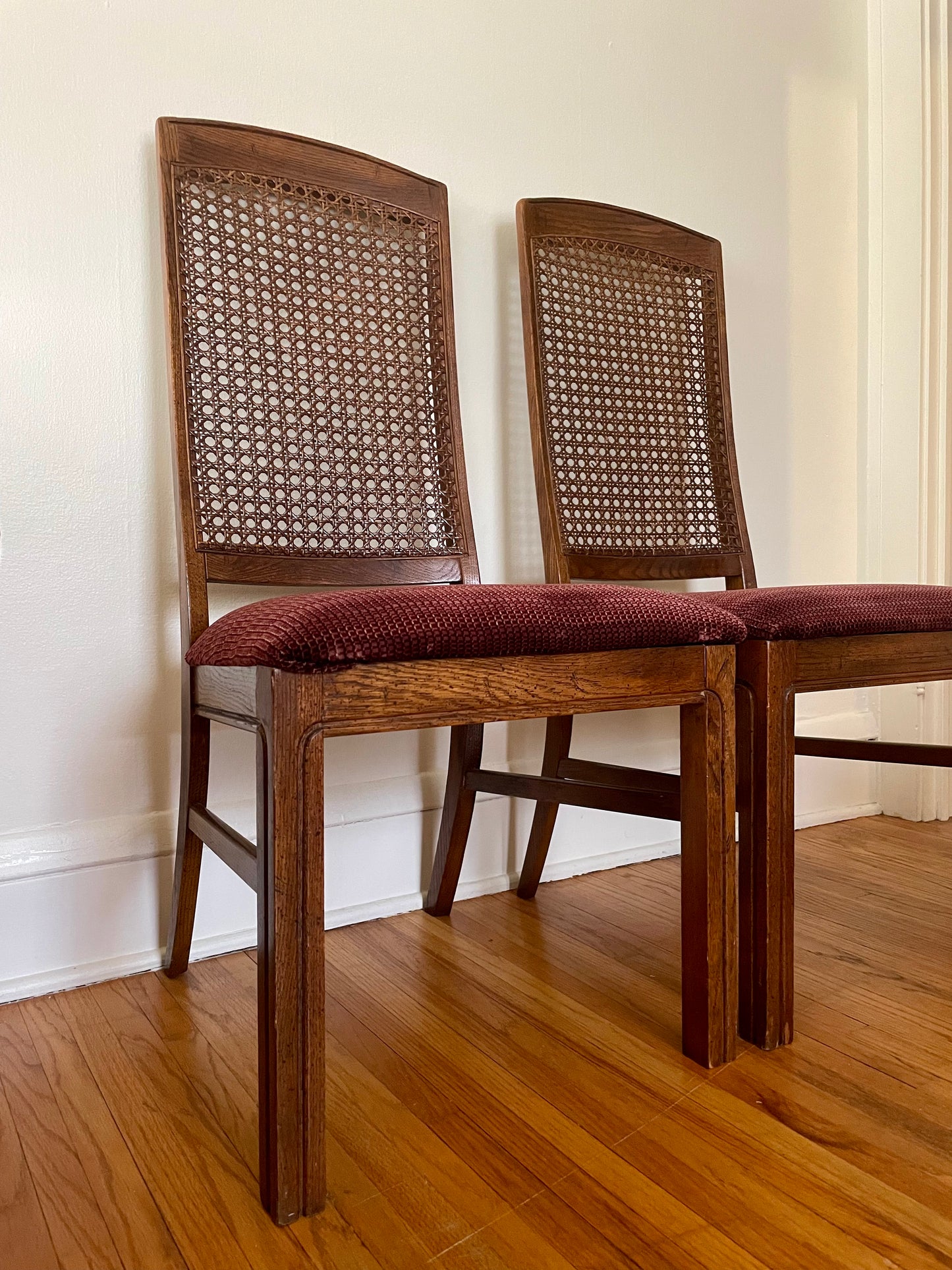 Two wooden chairs with cane backs and red cushions on a wooden floor.