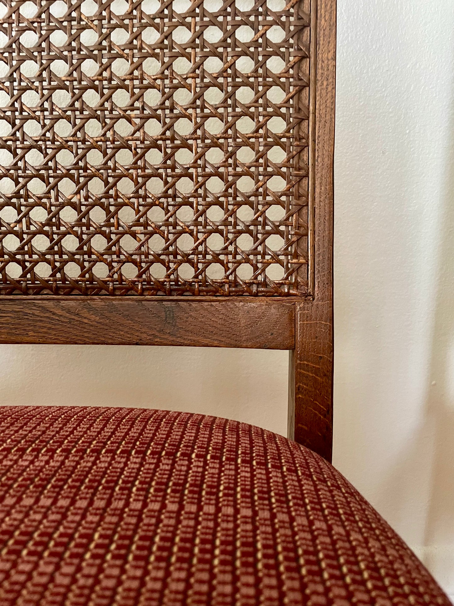 Wooden chair with cane backrest and red cushion against a white wall