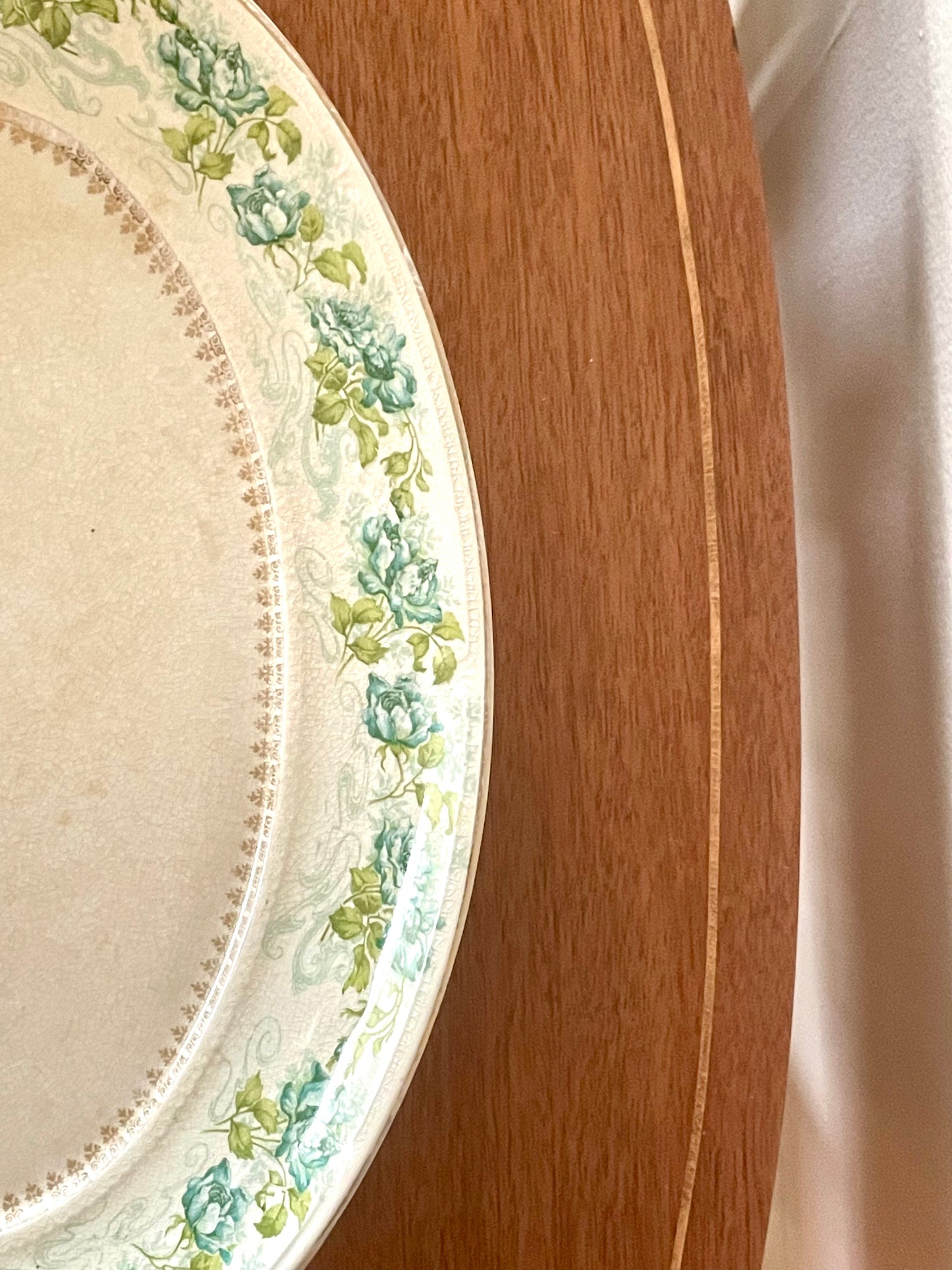 A close-up of a porcelain plate with a cream-colored center and a floral border featuring blue flowers and green leaves, resting on a wooden surface.