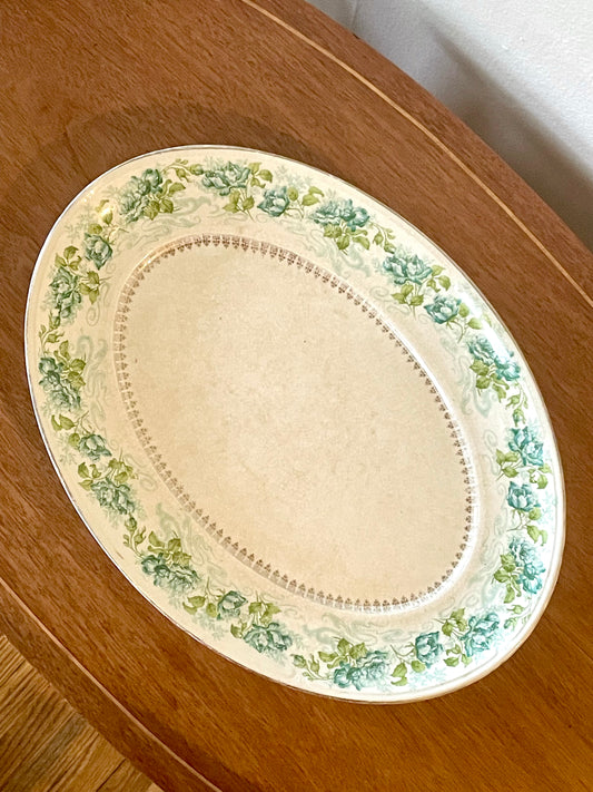 An oval porcelain serving platter with a floral border in green and blue, resting on a wooden table.