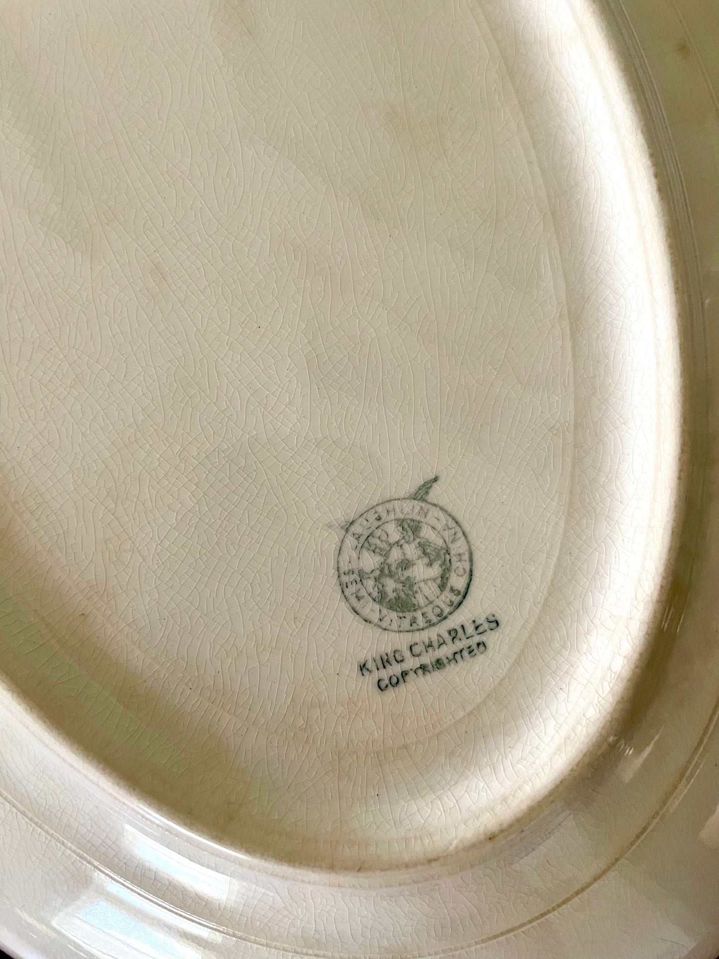 Close-up of the inside bottom of a white porcelain plate, showing a circular Laughlin China mark and the text ‘King Charles’ near the edge.