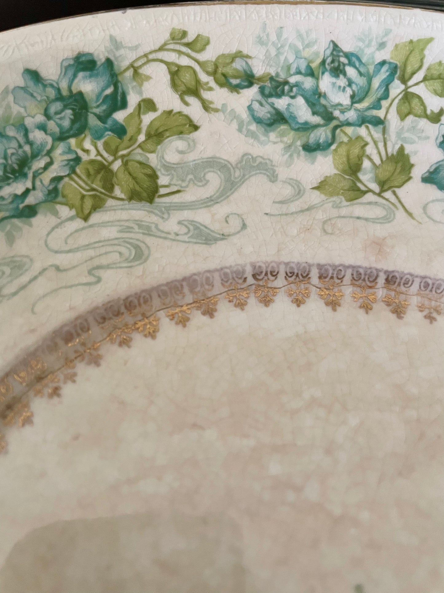 Close-up of an off-white decorative porcelain dish showing a floral border with blue-green roses and green leaves, plus a gold patterned rim.