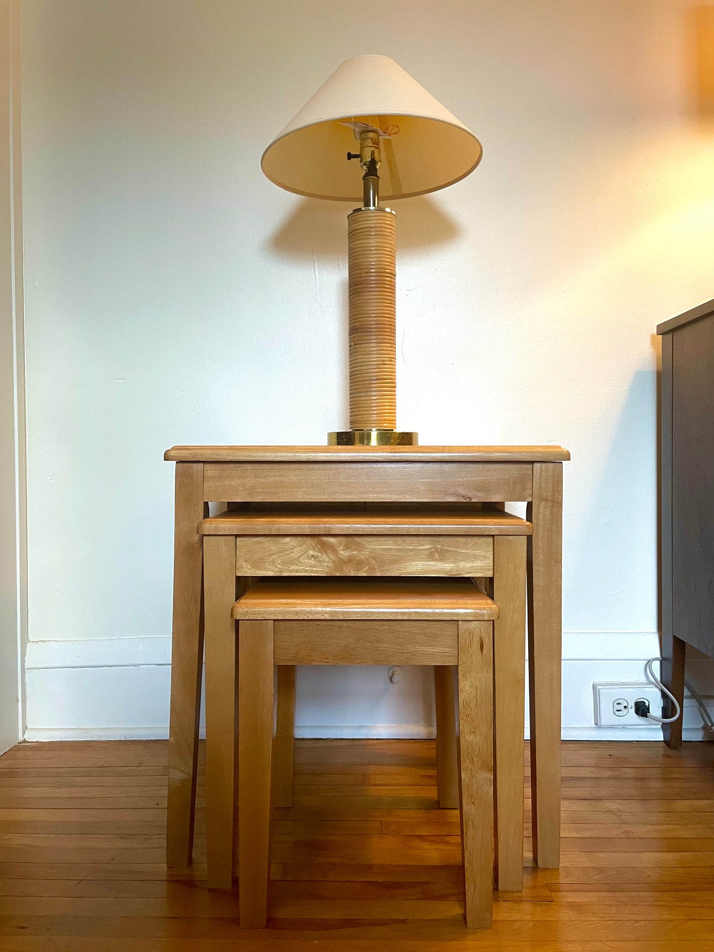 Set of wooden nesting tables with a lamp on top in a room setting.