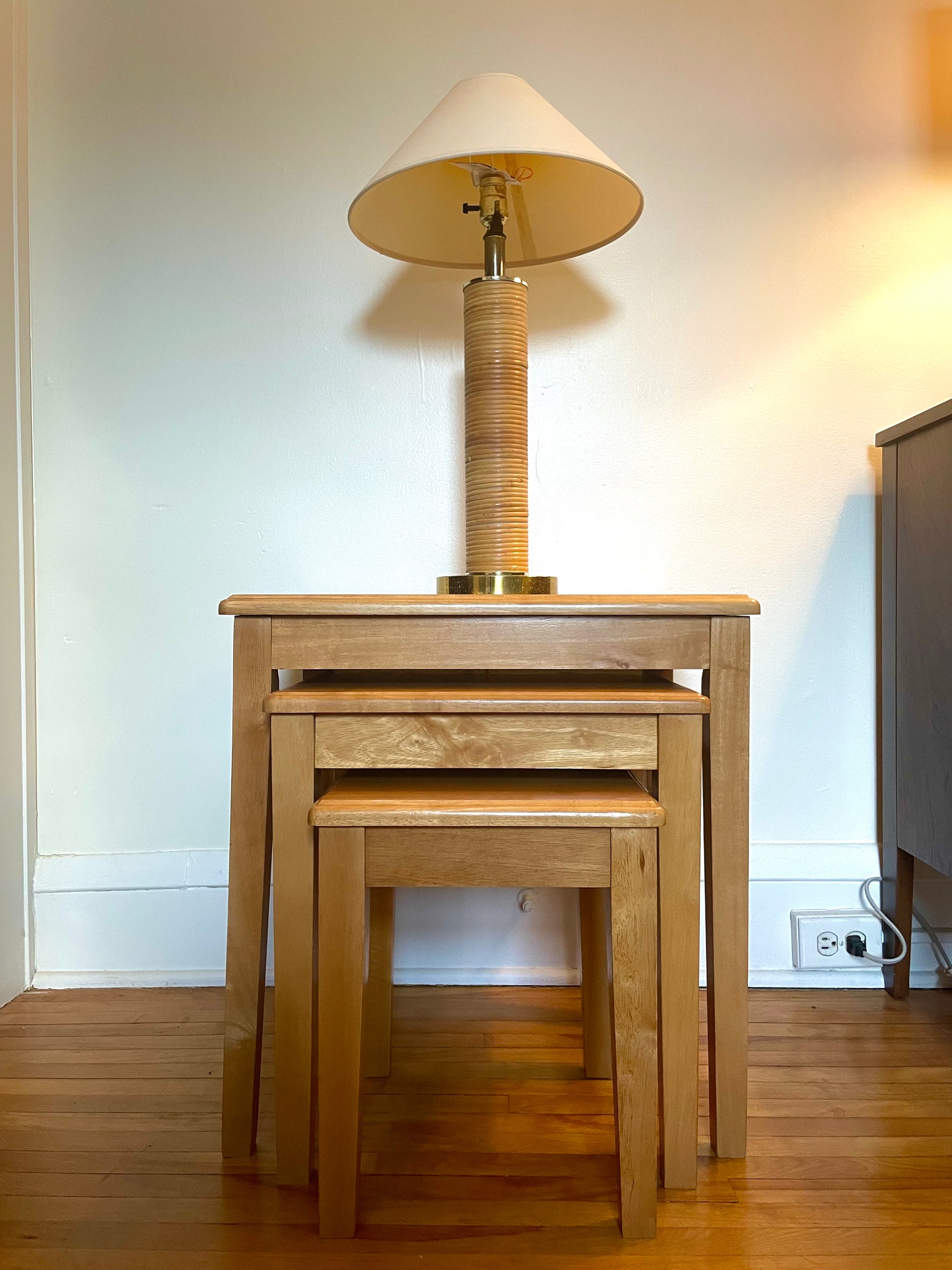 Set of wooden nesting tables with a lamp on top in a room setting.