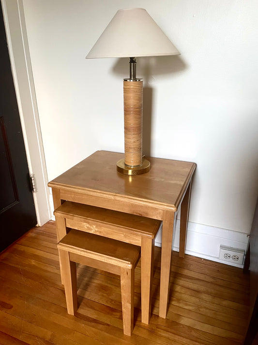 Set of wooden nesting tables with lower two tables slightly pulled out and a lamp on top against a white wall.