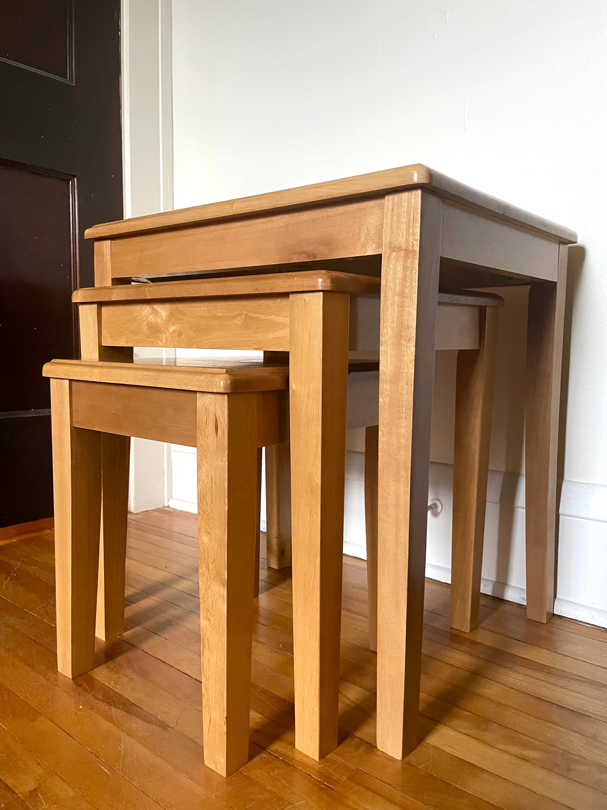 Set of three wooden nesting tables on a wooden floor.