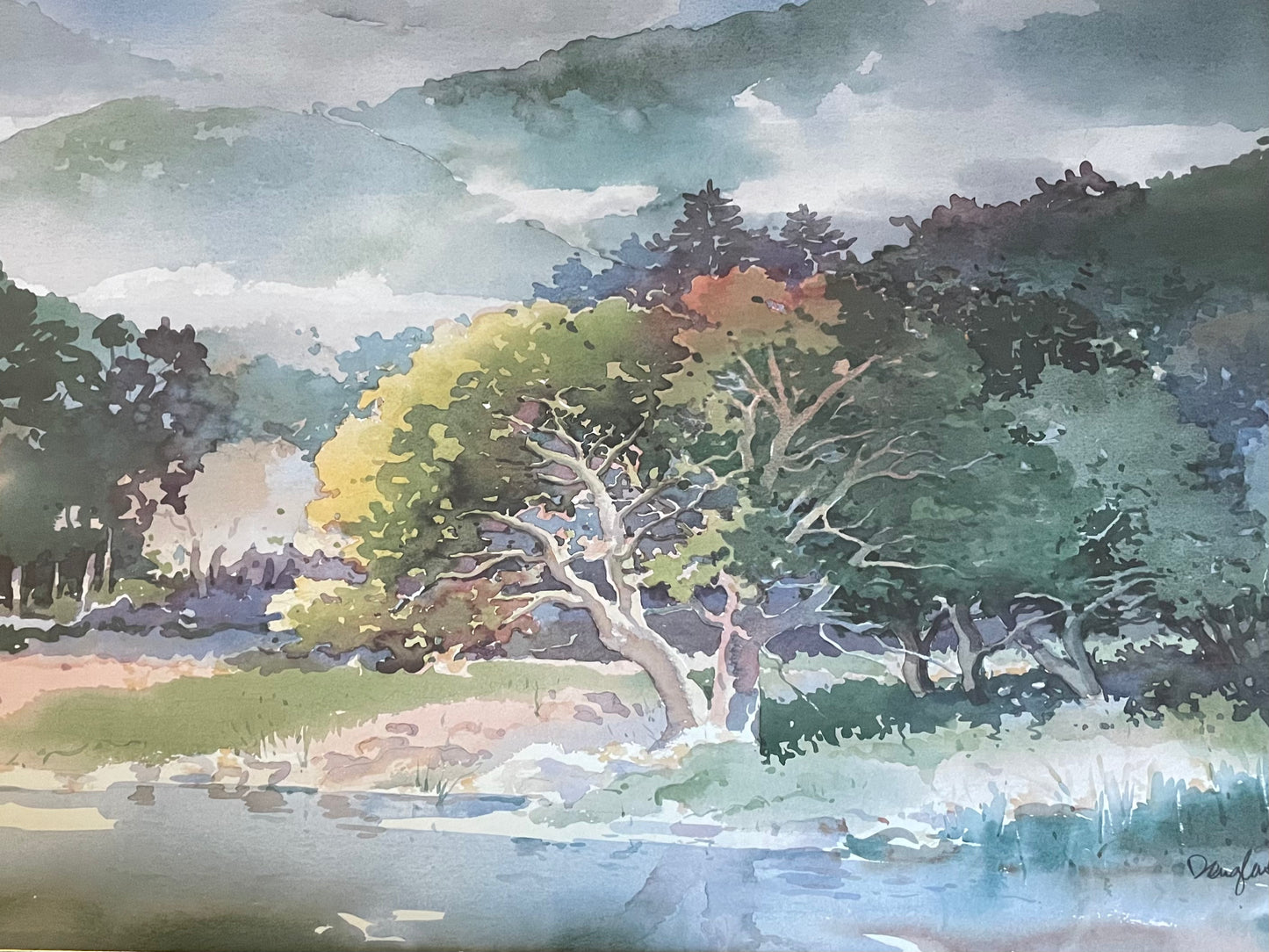 Watercolor landscape painting featuring a tree by a body of water, with green and yellow foliage, dark forested hills, and a cloudy sky.