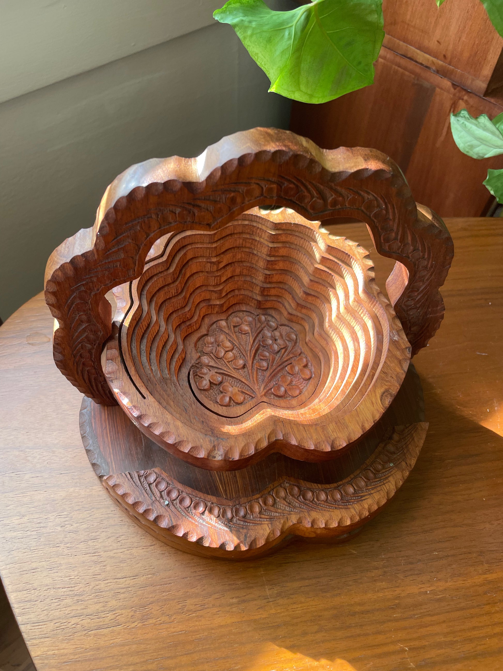 Wooden tiered basket with intricate carvings and a handle, set on a wooden surface.