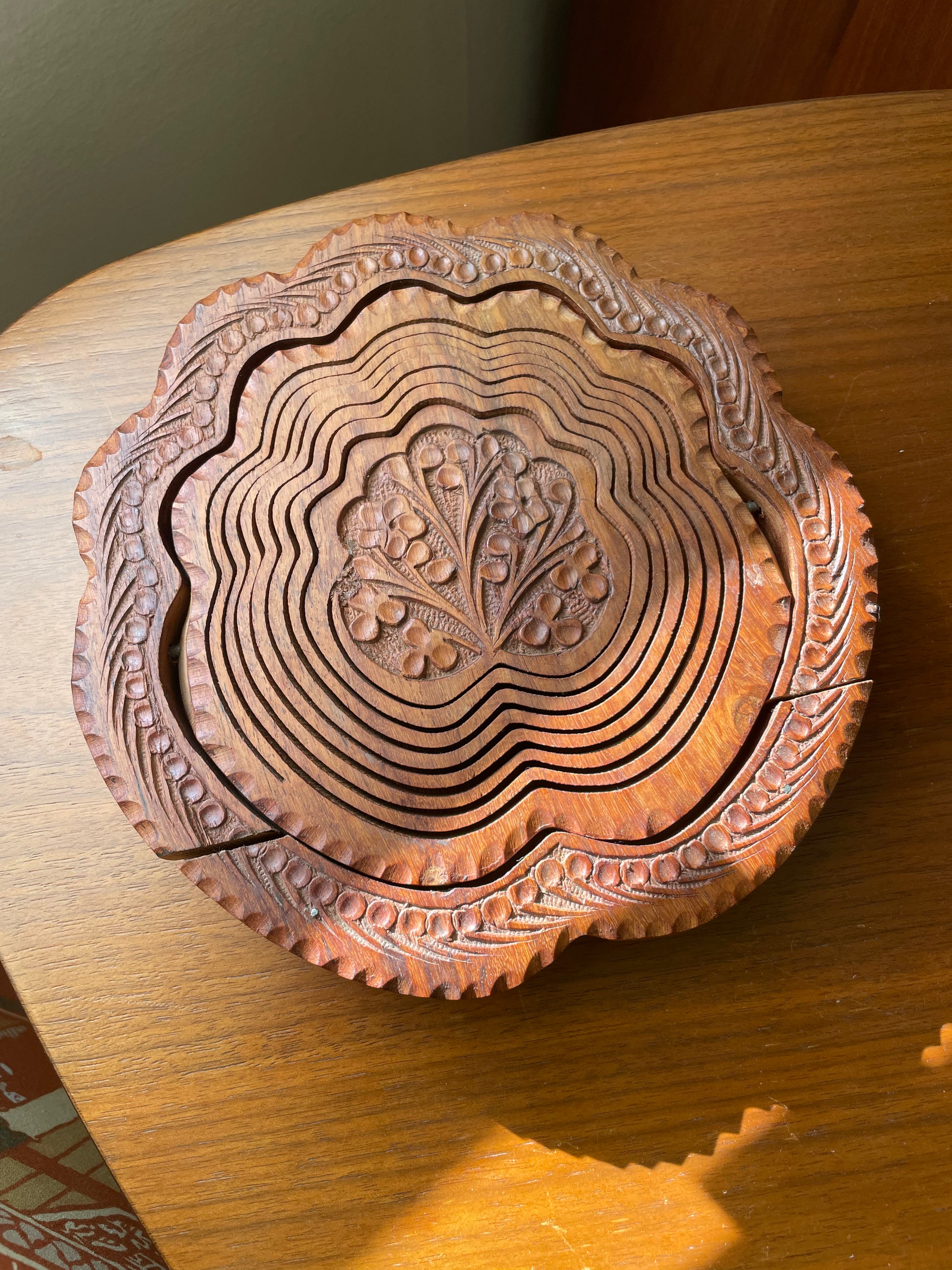 Round wooden trivet with scalloped edges and carved floral patterns.