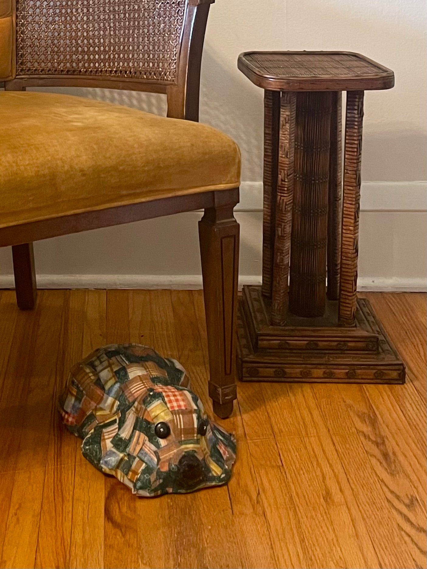 A decorative ceramic dog figurine with a colorful patchwork quilt pattern sits on a hardwood floor next to a wooden chair and a dark wood side table.
