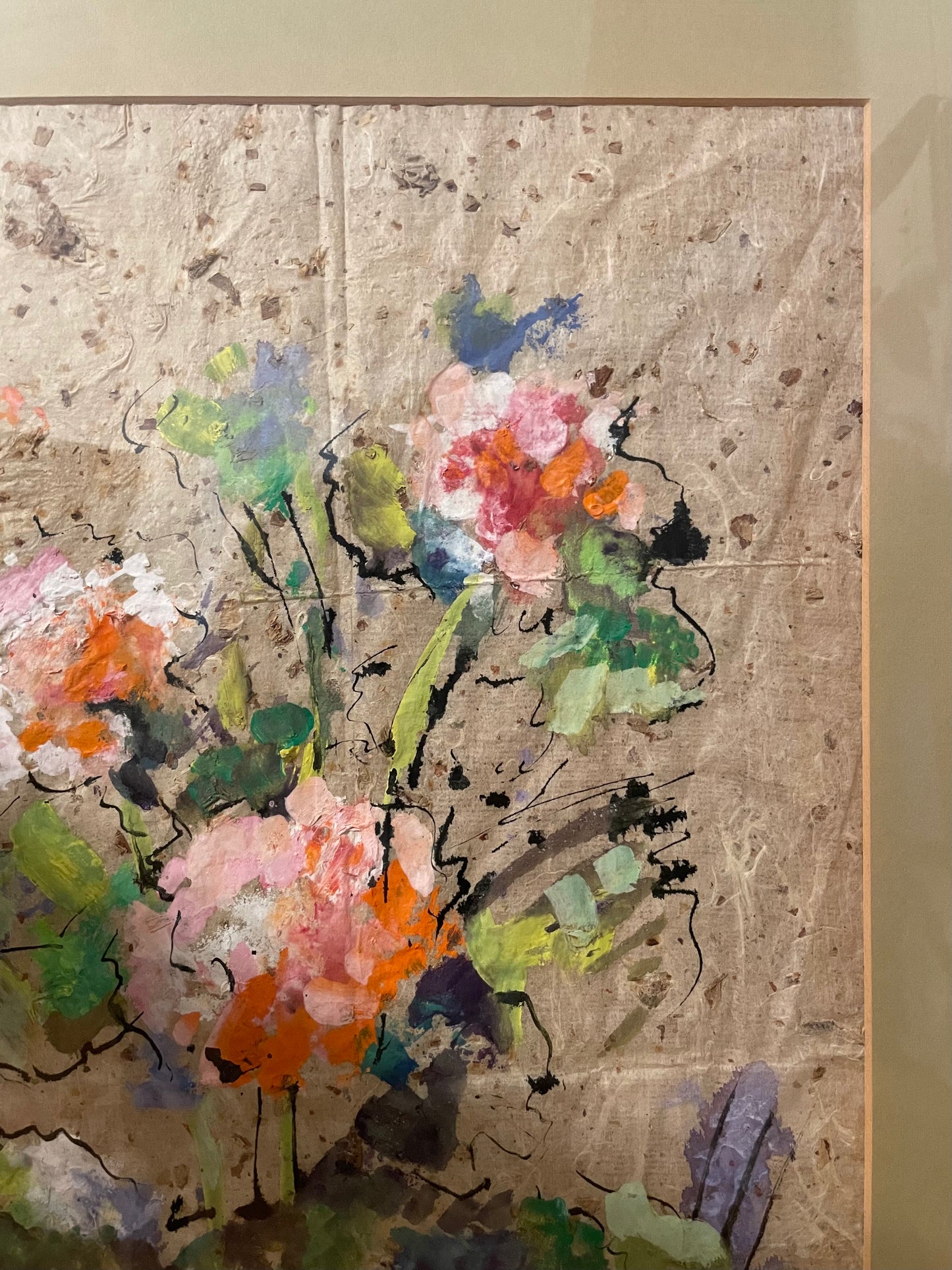 An abstract floral painting on textured beige paper, featuring expressive brushstrokes in pink, orange, green, blue, and black, framed by a beige mat.