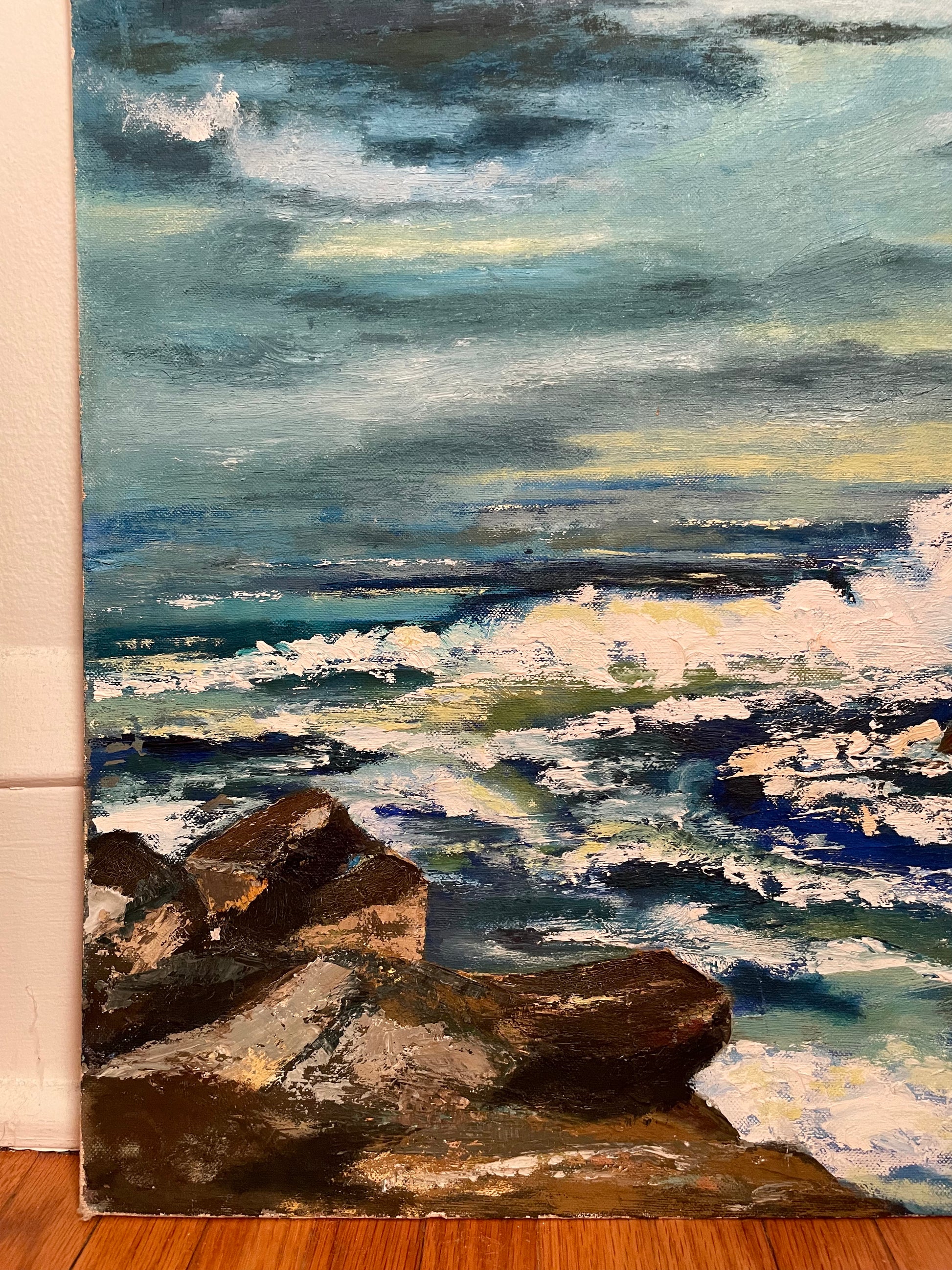 An impressionistic oil painting of a dramatic ocean scene with dark rocks in the foreground, white surf, and a cloudy sky in shades of blue, gray, and green.