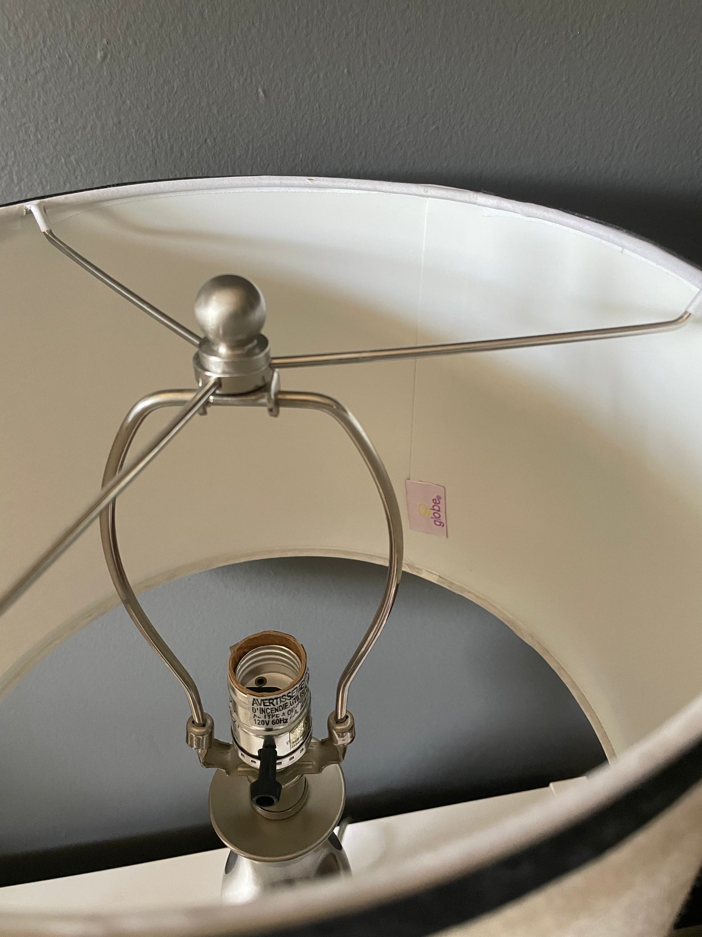 Close-up of a lampshade interior with a silver metal lamp support and visible bulb socket, set against a dark gray wall.