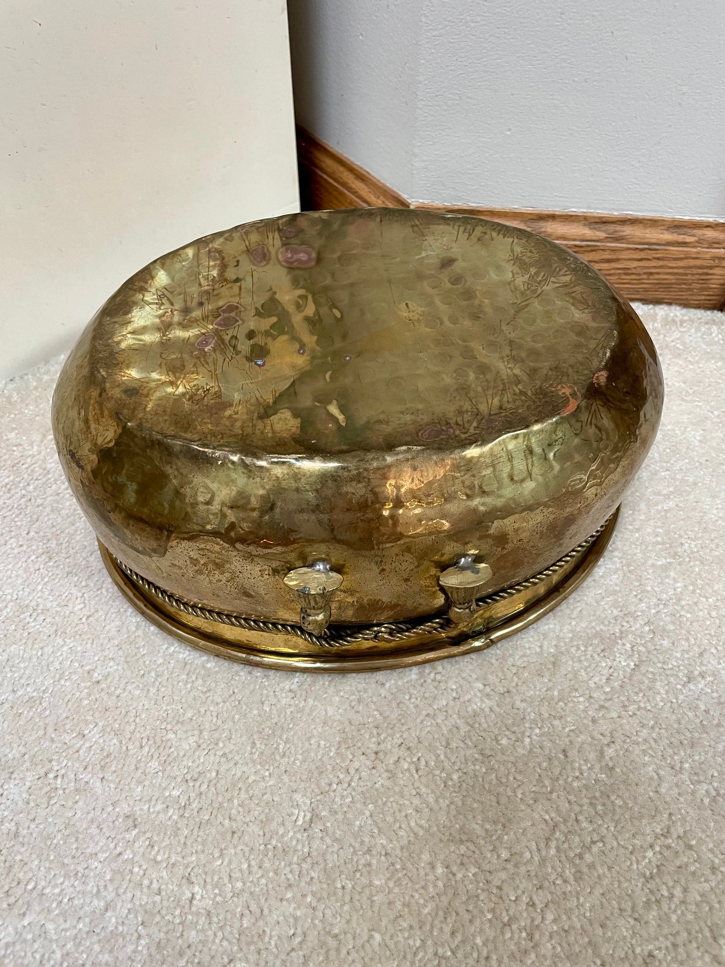 Underside of brass pot with hammered texture and faux ropes with tassels knotted at the front.