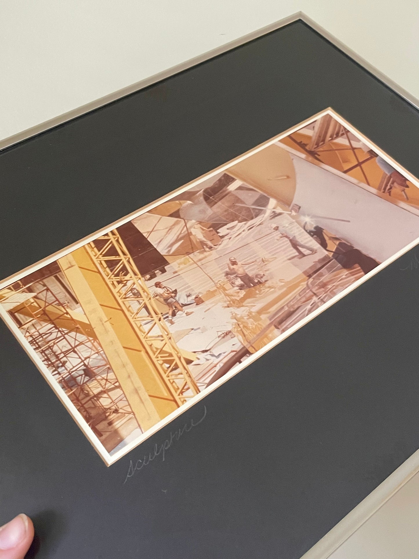 A framed art print featuring a yellow and sepia-toned photograph of construction workers on a building site, mounted on a wide black mat board with a silver frame.