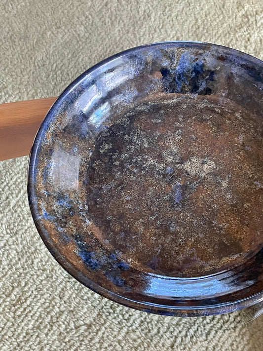 A large round ceramic bowl with speckled blue and brown glazing rests on a glass table over a blue-grey rug.