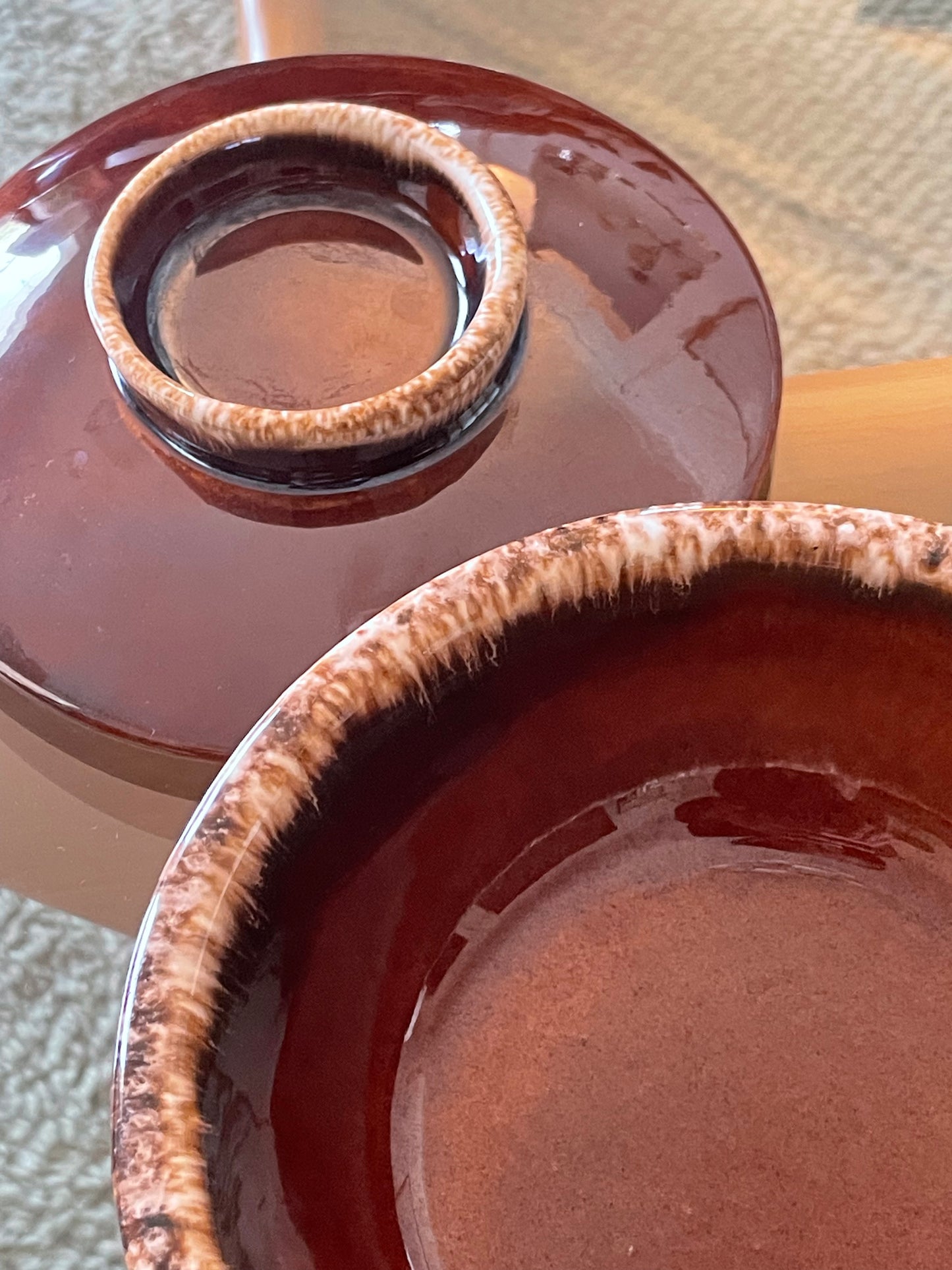 Close-up of a glossy ceramic bowl with a matching lid, both in a deep reddish-brown glaze with a contrasting speckled cream and brown rim.