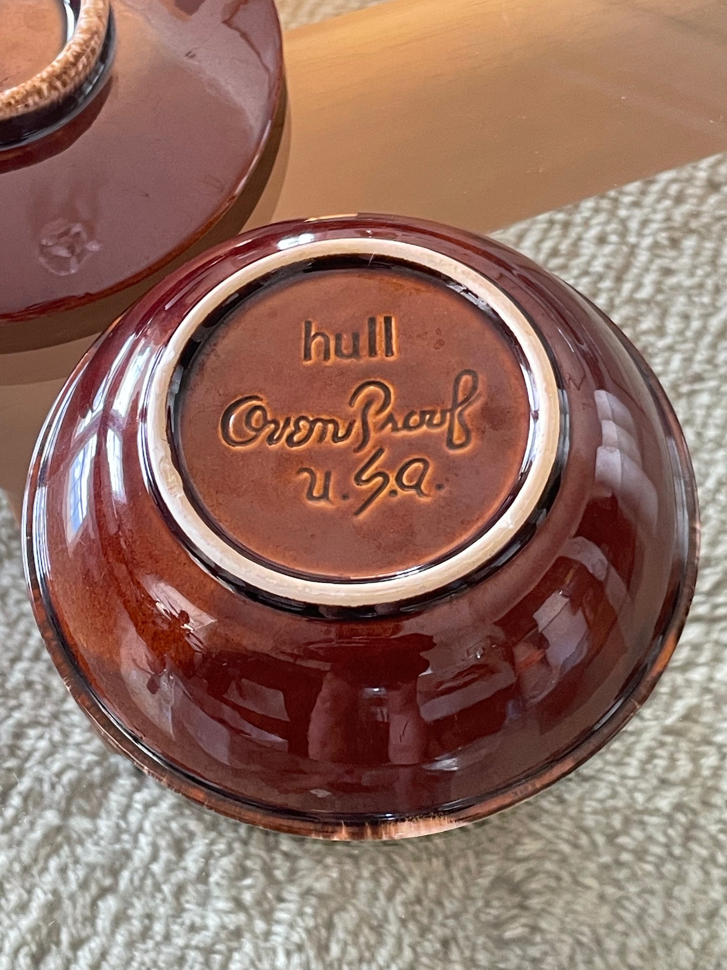 A close-up of the bottom of a glossy reddish-brown ceramic bowl, showing the embossed brand name 'hull' and 'Oven Proof USA'.