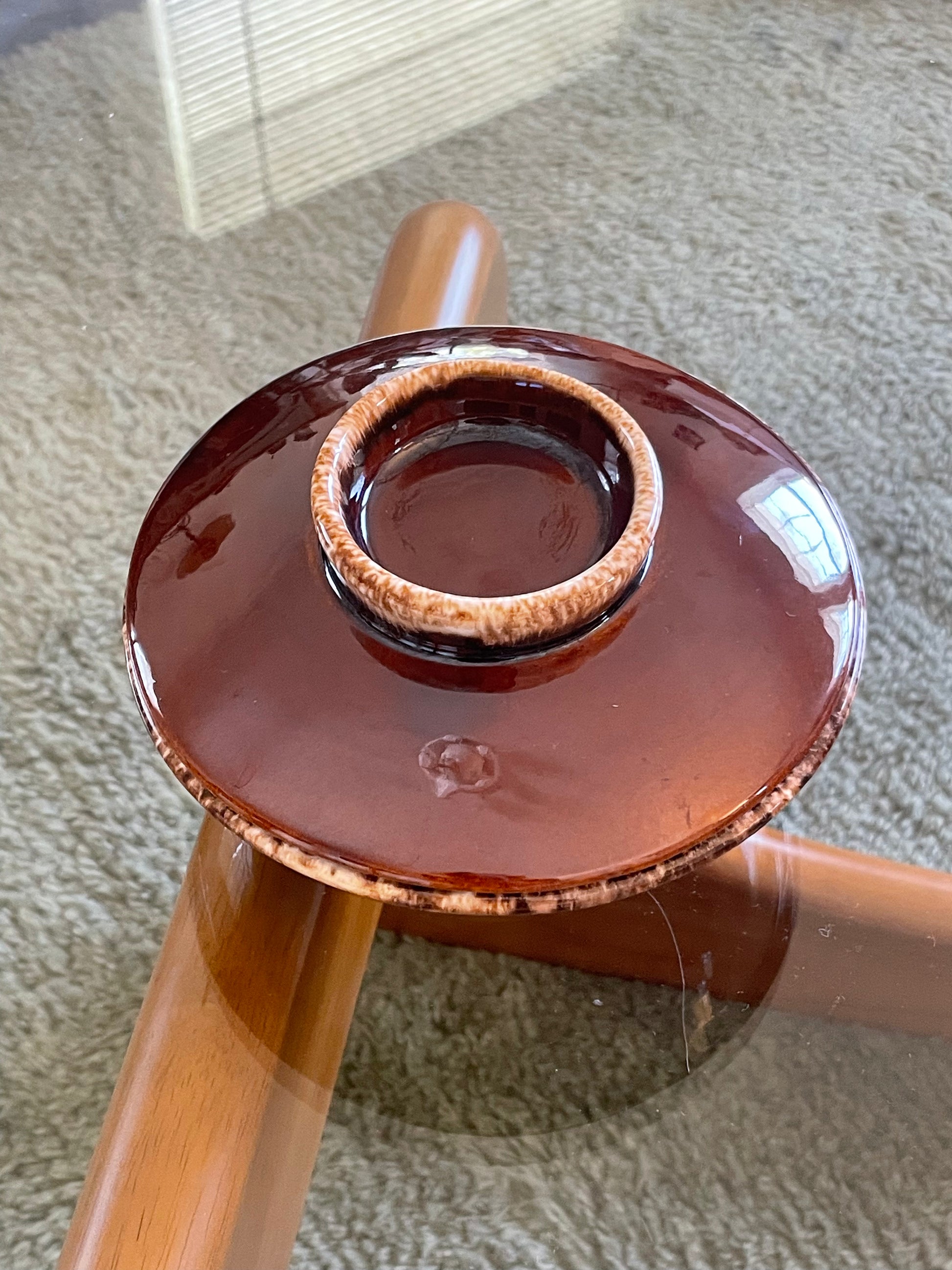 A round glossy ceramic bowl with a lid, shown resting on a glass-top wooden table over a carpeted floor.