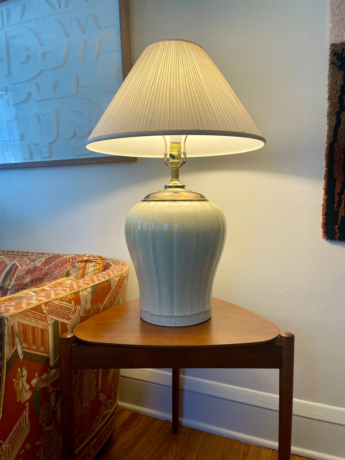 A table lamp with a white fabric pleated shade and a glossy pale yellow ceramic base, illuminated and placed on a wooden side table in a living room setting.