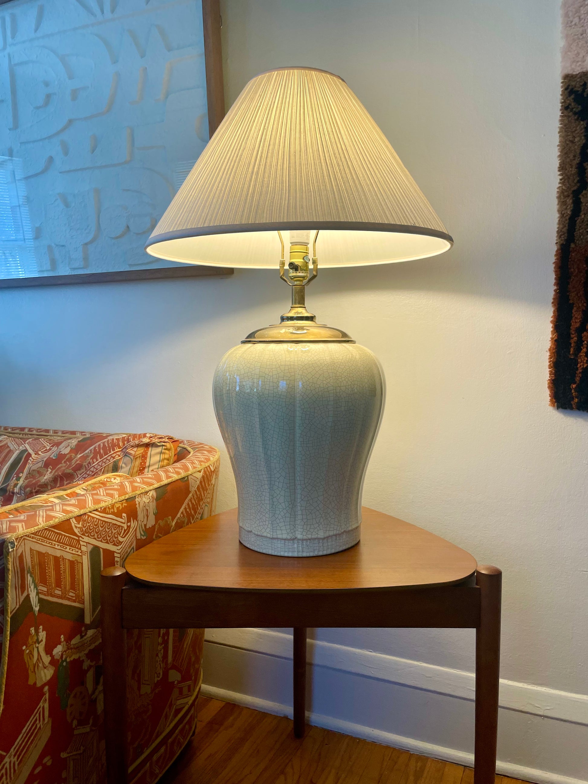 A table lamp with a white fabric pleated shade and a glossy pale yellow ceramic base, illuminated and placed on a wooden side table in a living room setting.