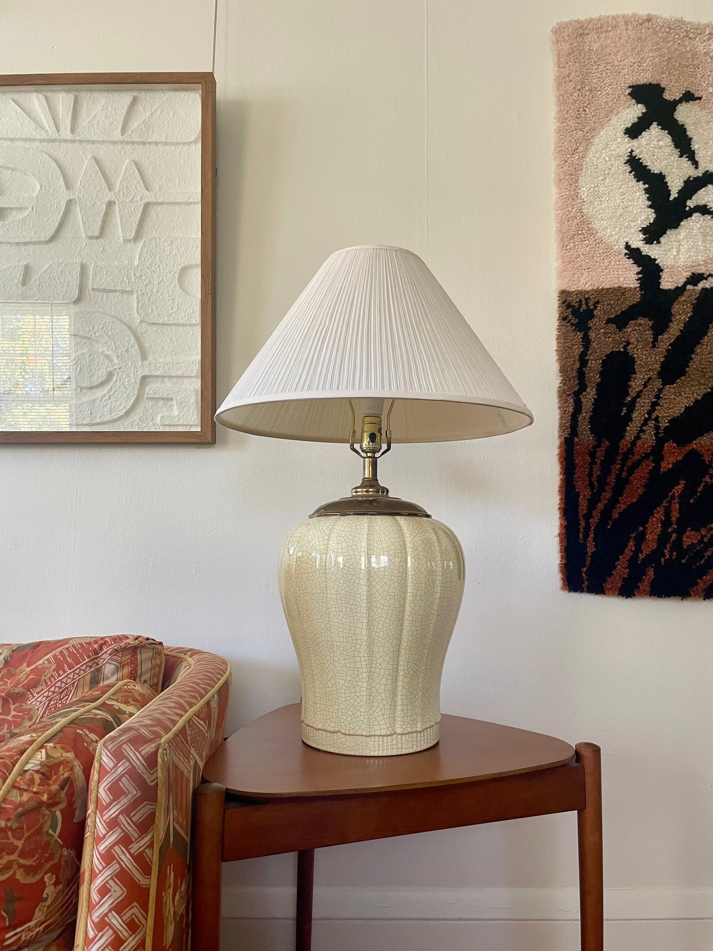 A table lamp with a ribbed cream ceramic base and a pleated white shade, styled on a wooden side table in a home interior setting.
