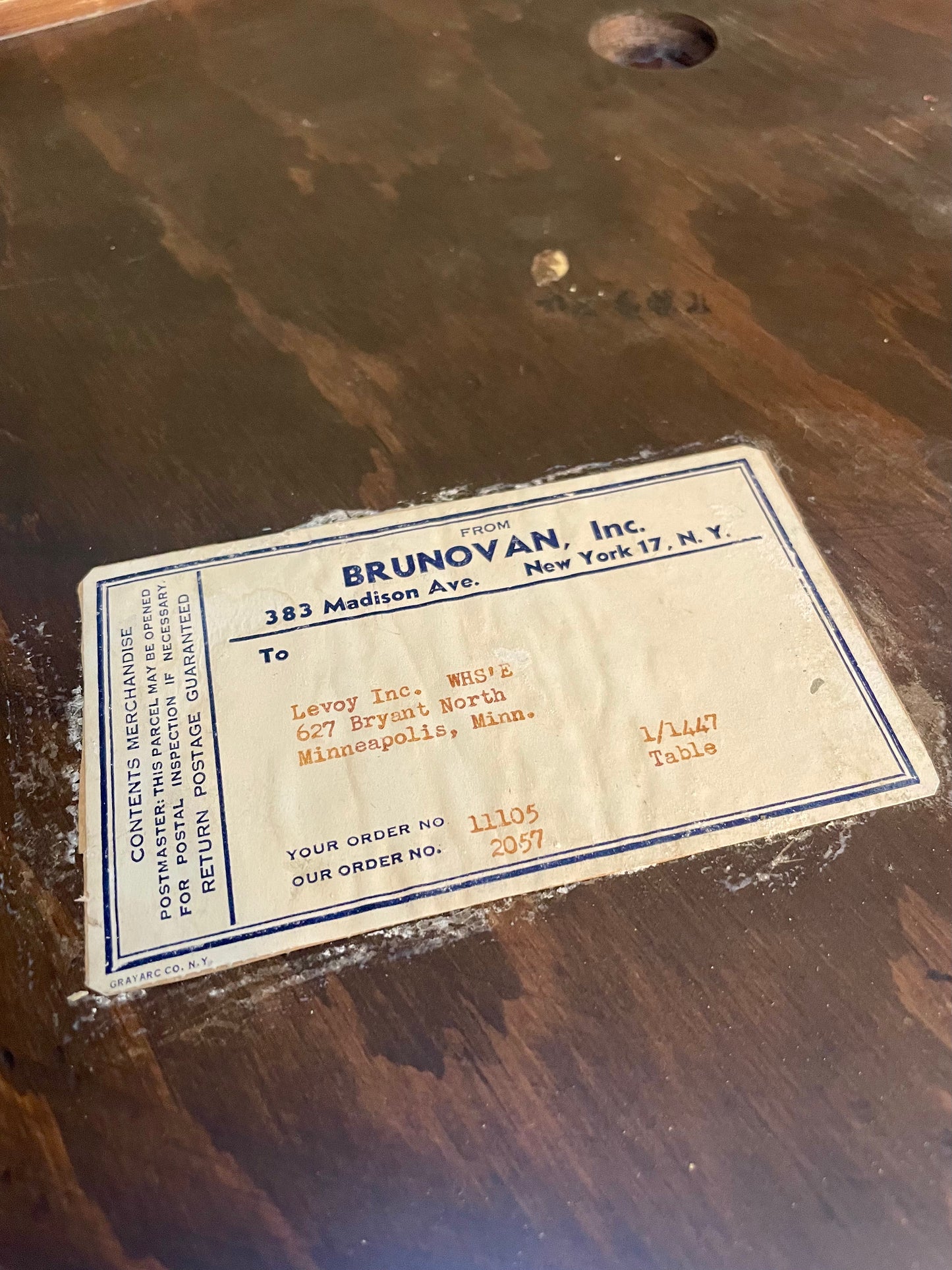 A vintage paper shipping label from 'Brunovan, Inc.' placed on a dark wooden surface.