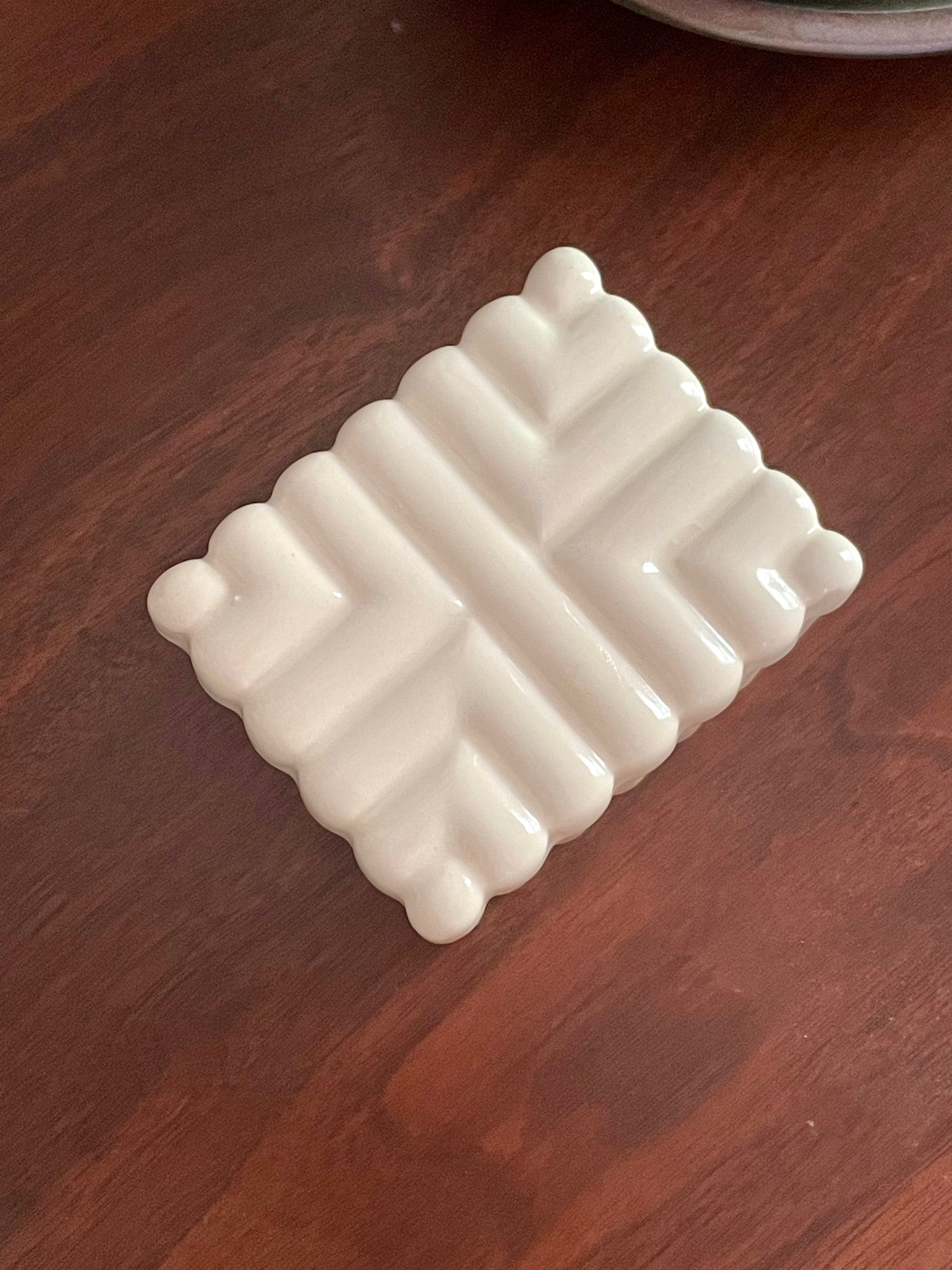 Overhead view of an off-white ceramic rectangular box with a raised geometric pattern, resting on a dark brown wooden surface.