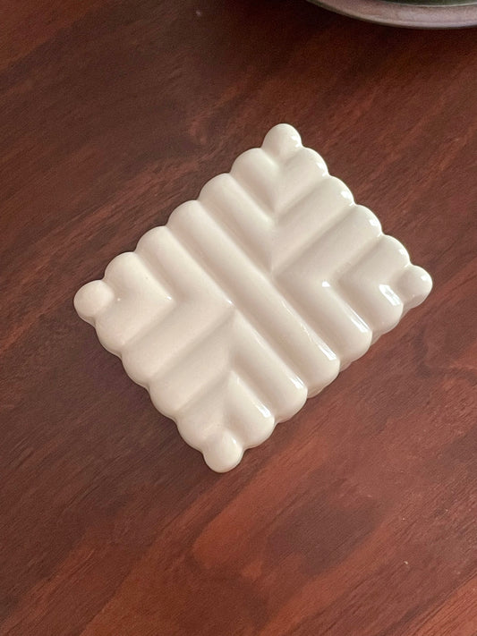 Overhead view of an off-white ceramic rectangular box with a raised geometric pattern, resting on a dark brown wooden surface.