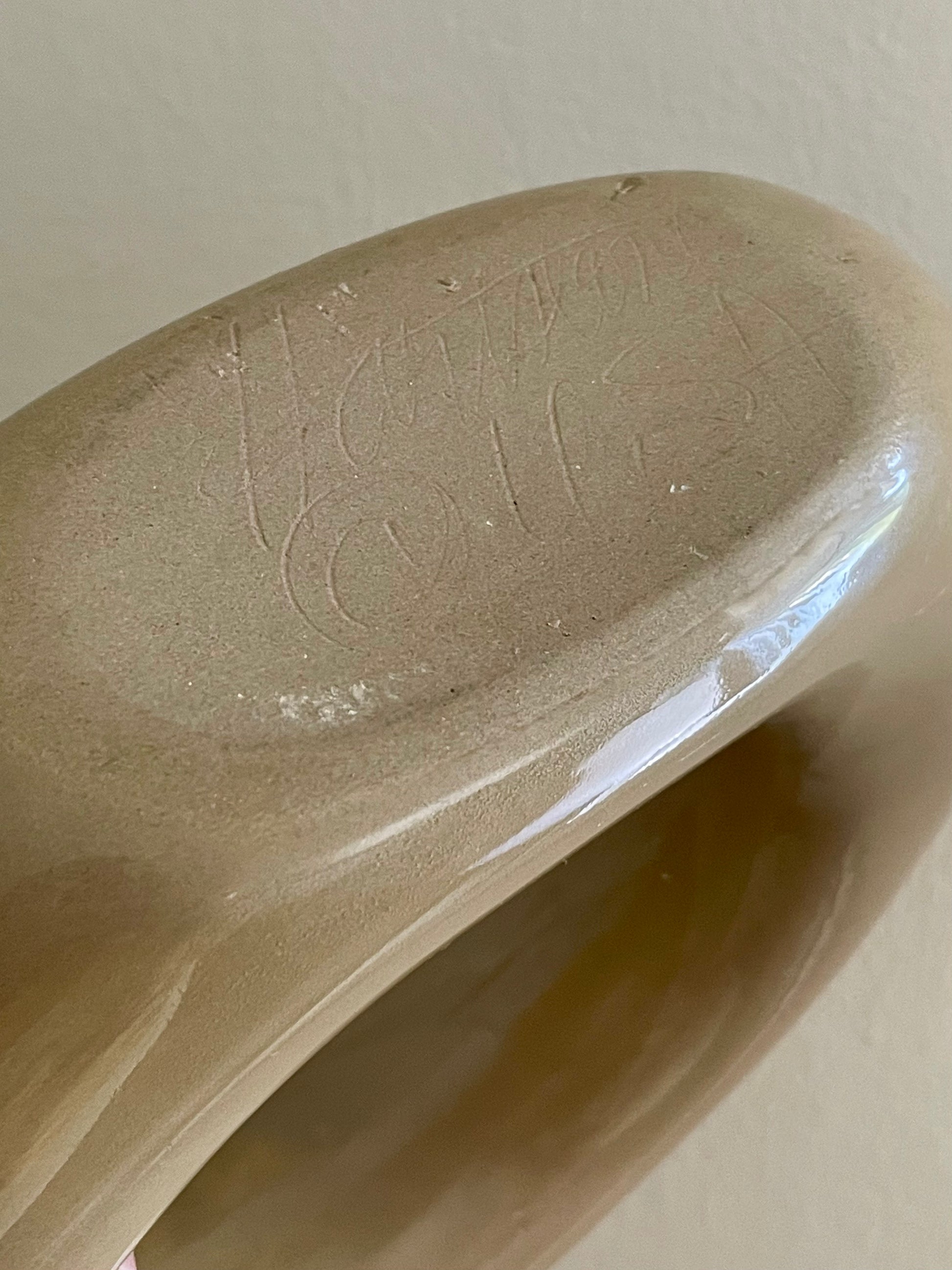 Close-up of the underside of a glossy beige ceramic decanter, showing a faint hand-written signature of ‘Hartstone USA’, against a plain light background.