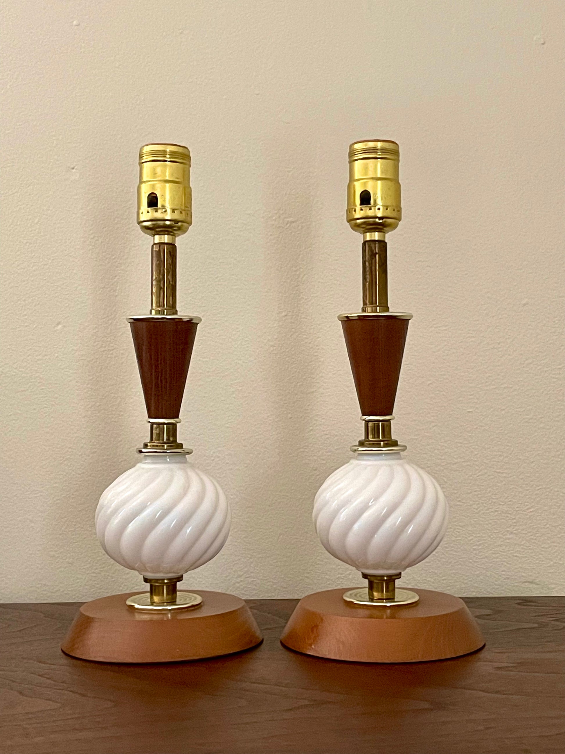 A pair of mid-century modern table lamps with white ribbed glass globes, dark brown conical necks, and warm brown wooden bases, set against a plain beige wall.