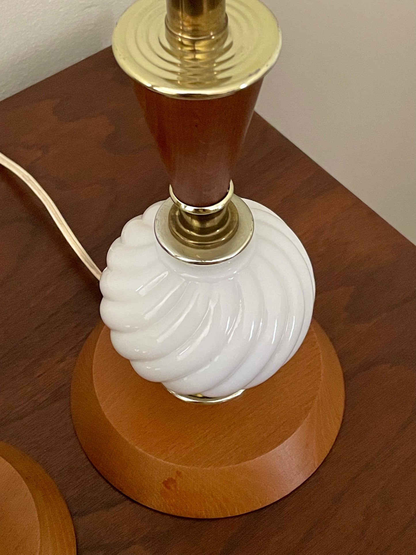 Closeup of a vintage table lamp with a ribbed white glass globe, a warm brown wood neck, and polished gold-toned metal accents, sitting on a wooden surface.