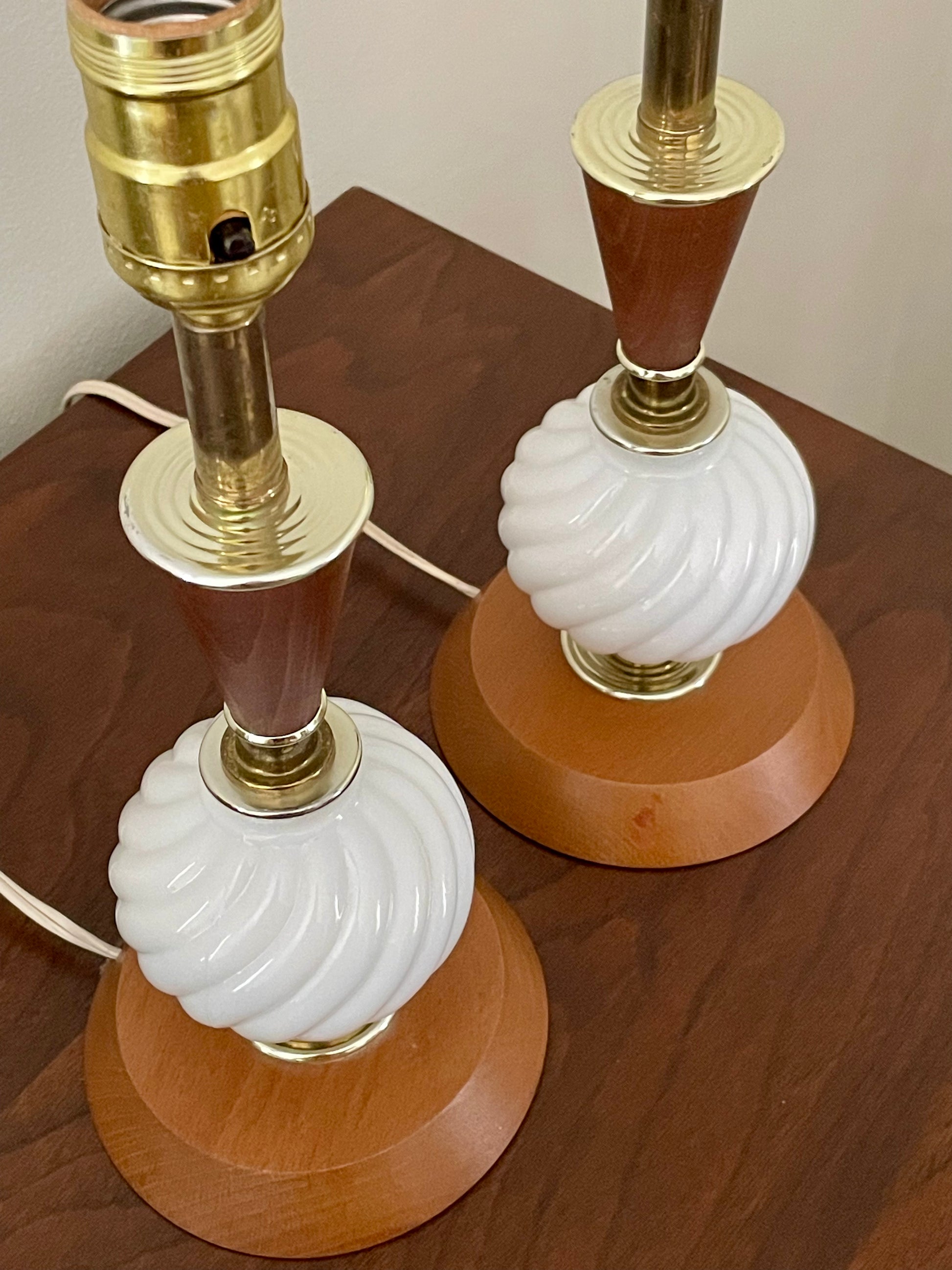 A pair of vintage table lamps with white ribbed glass globes, medium brown wood accents, and brass-colored metal bases, shown on a dark wood tabletop.