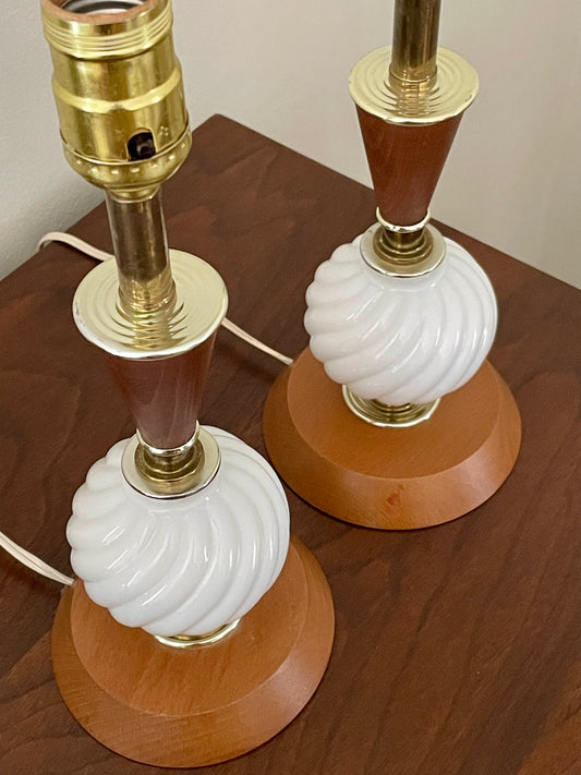A pair of vintage table lamps with white ribbed glass globes, medium brown wood accents, and brass-colored metal bases, shown on a dark wood tabletop.