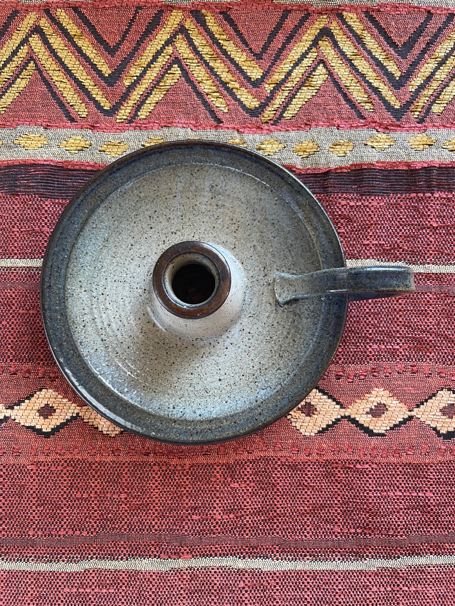 View from above of a circular ceramic candle holder with handle, resting on a Southwest patterned fabric.