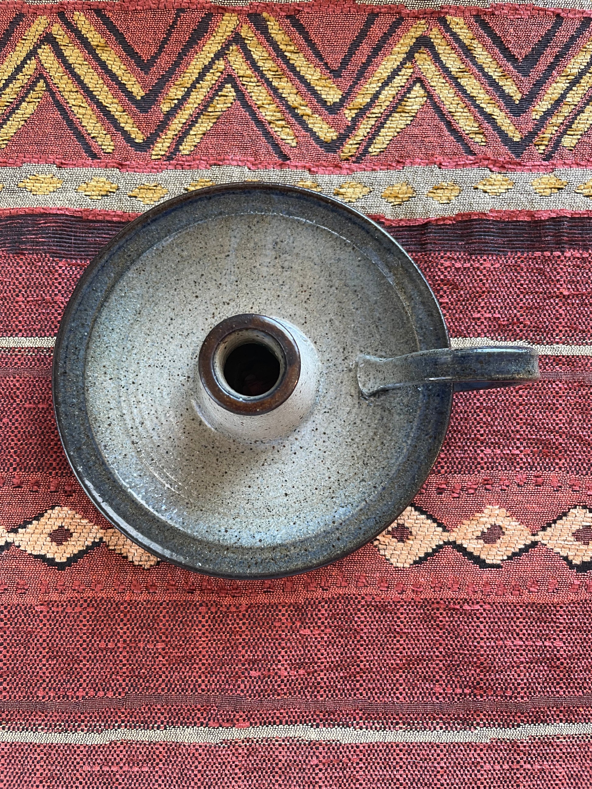 View from above of a circular ceramic candle holder with handle, resting on a Southwest patterned fabric.