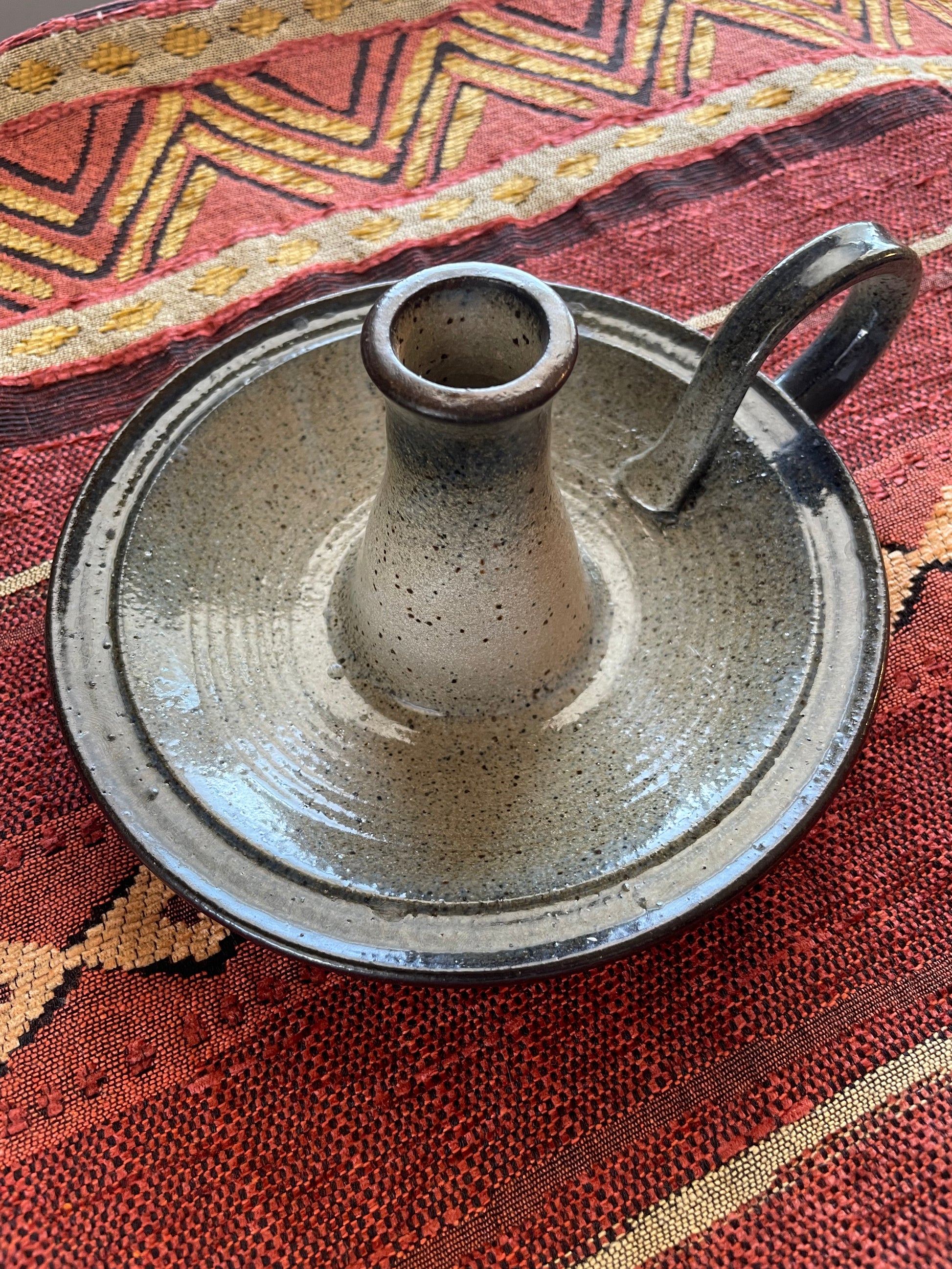 Ceramic candle holder with handle on a Southwest patterned fabric background.