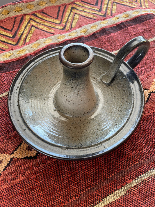 Ceramic candle holder with handle on a Southwest patterned fabric background.
