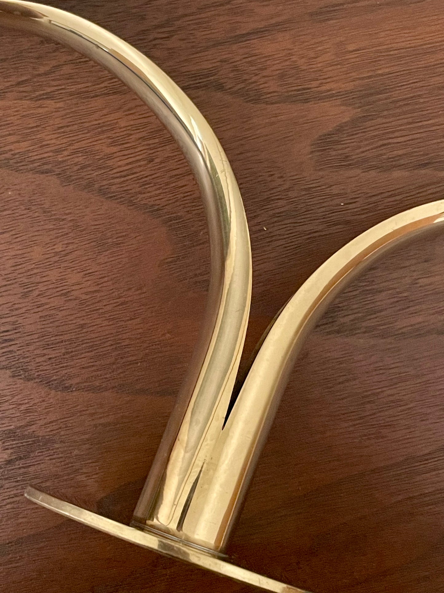 A close-up of a polished brass candleholder with a curved design and circular base, resting on its side on a dark wood surface.